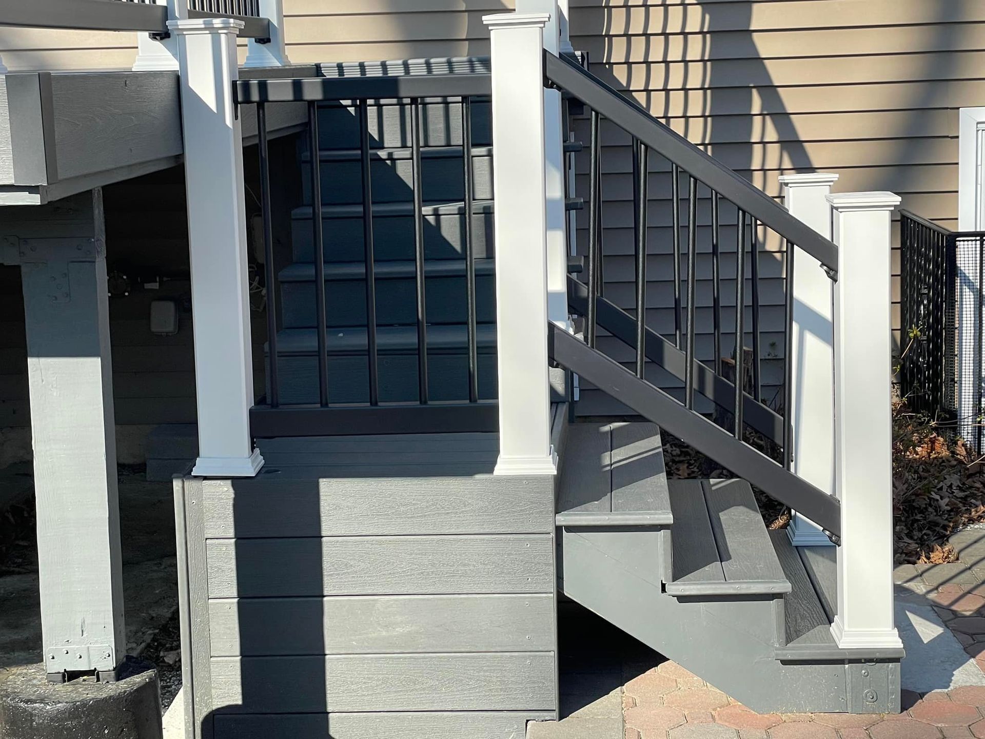 Grey composite deck stairs with black railing and white posts next to a beige building.