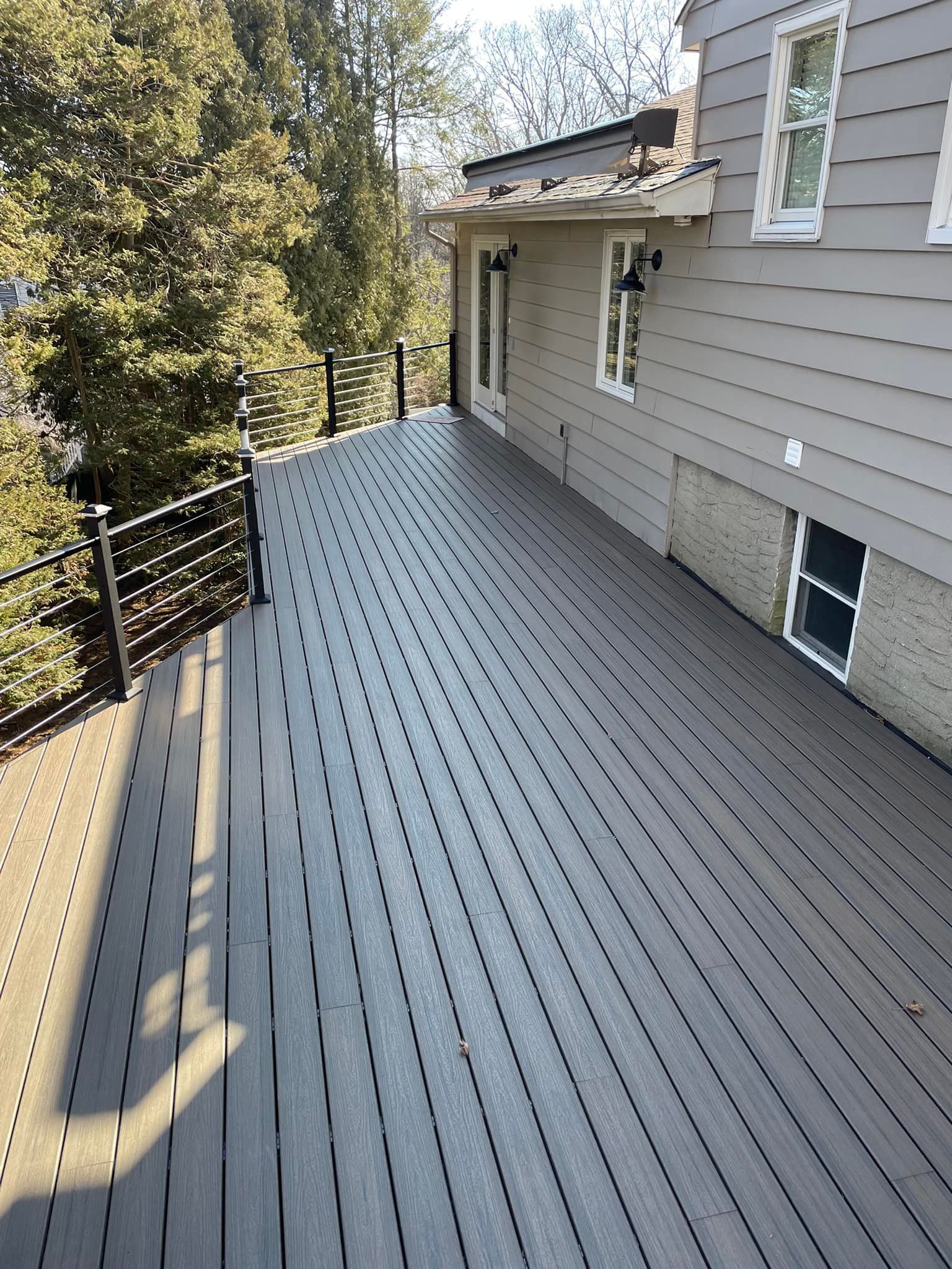 Grey composite deck with black railing next to a house with beige siding and windows.