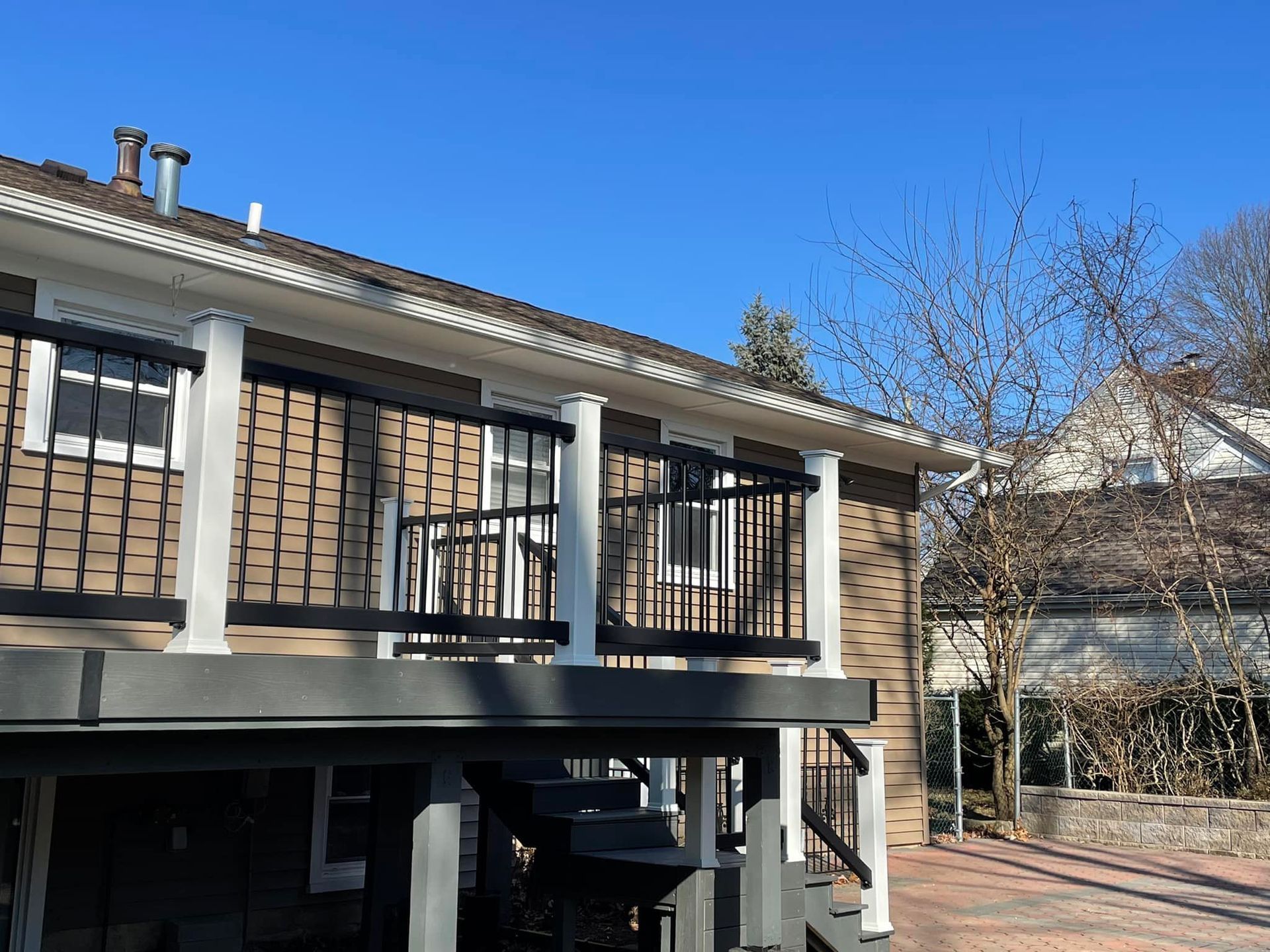 Exterior view of a house with a deck. Brown siding, white trim, black railing, blue sky.