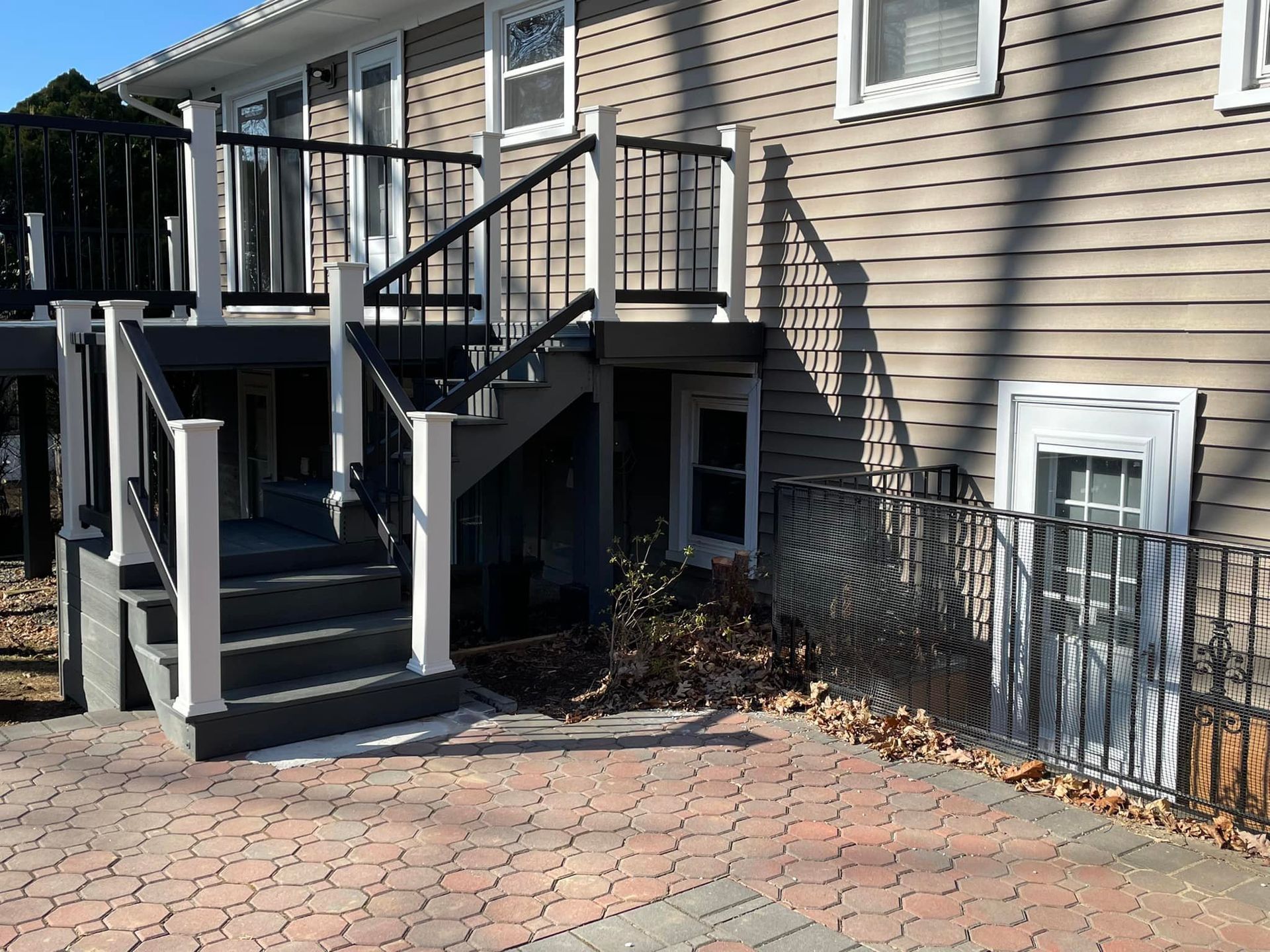 Deck and stairs with black and white railings leading to a house with beige siding and a lower level door.