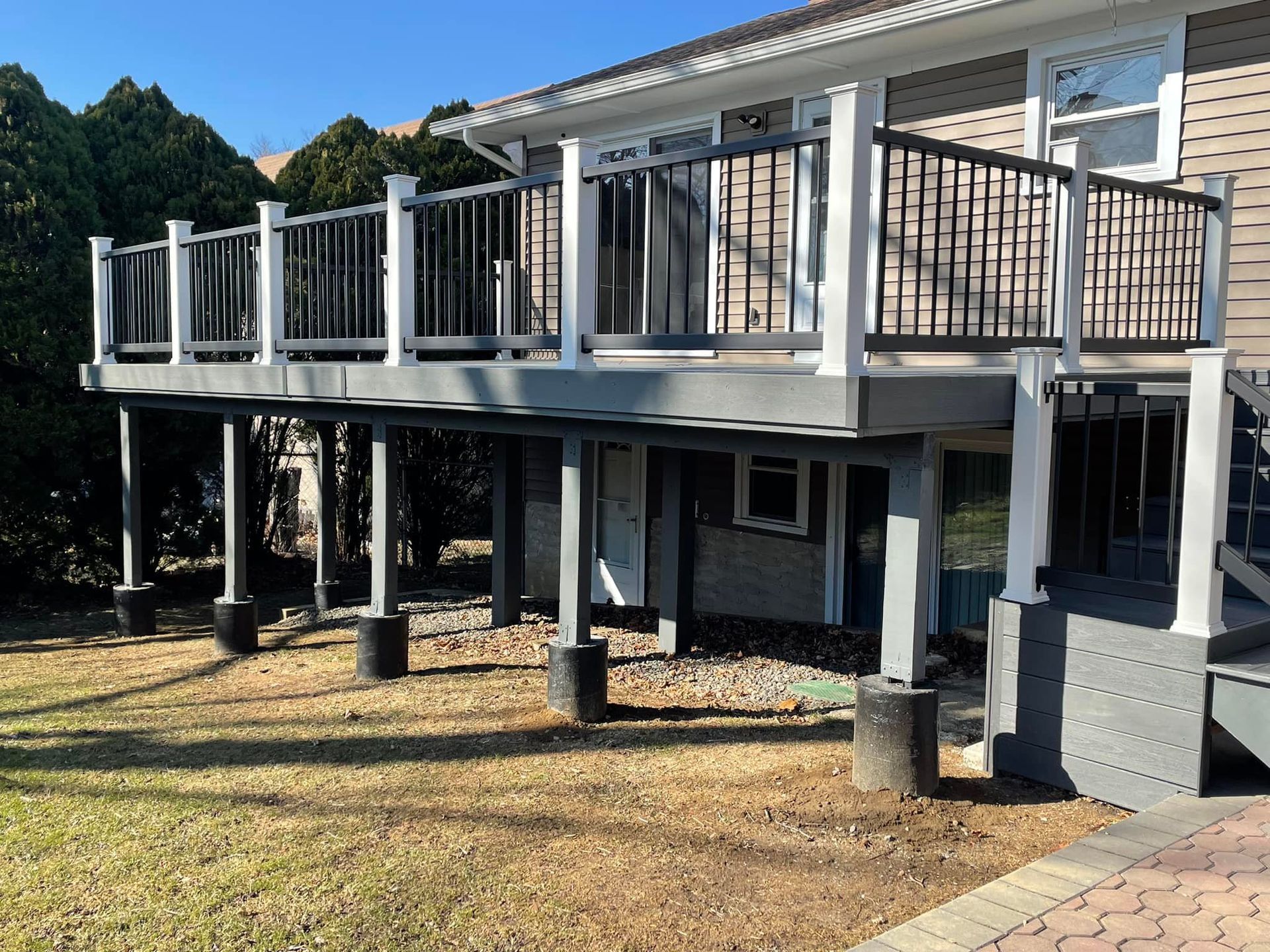 Elevated deck with white posts, black railings, and gray flooring; attached to a house with beige siding.