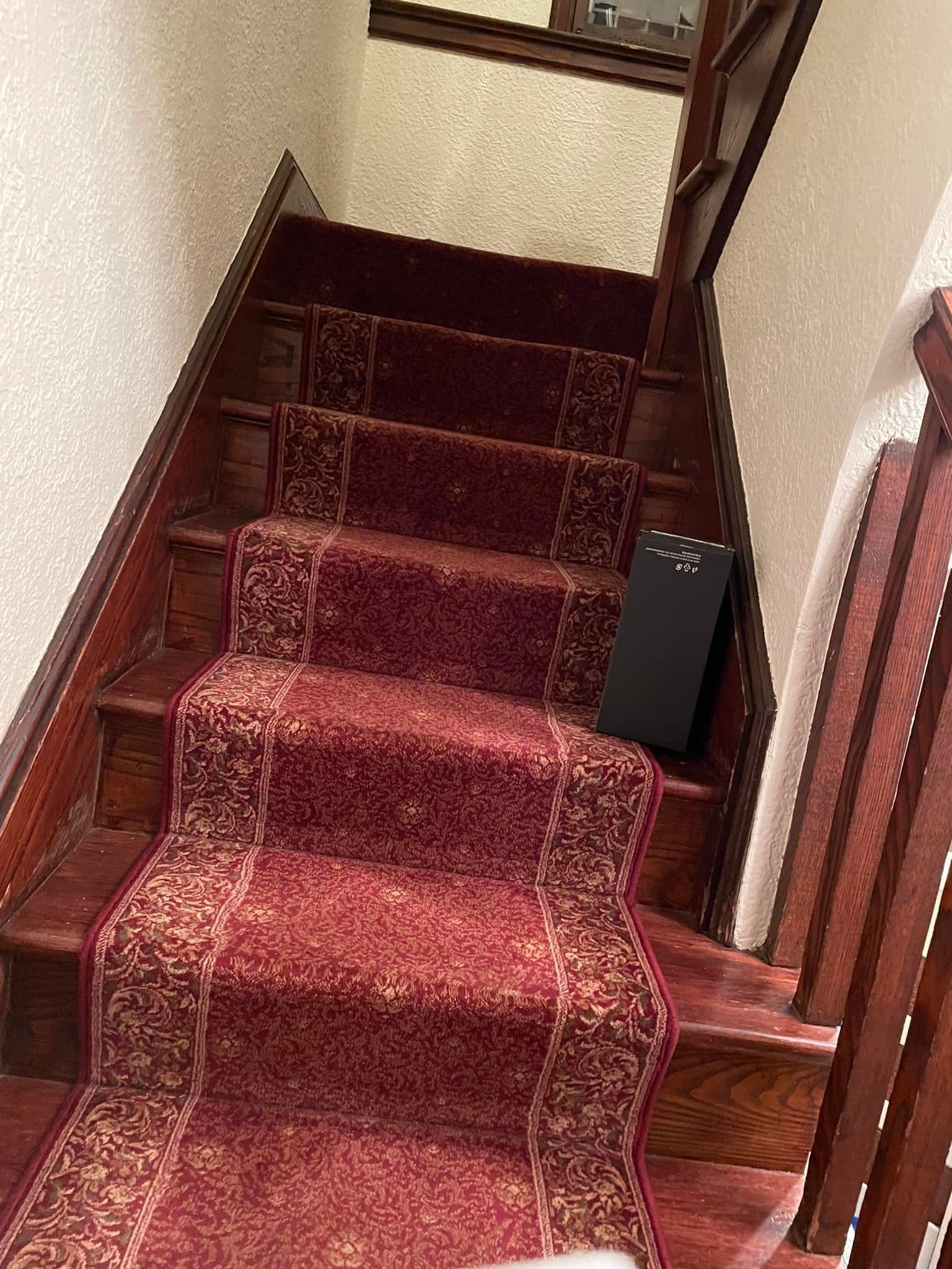 Wooden staircase with red patterned carpet runner. A black rectangle rests on a step.