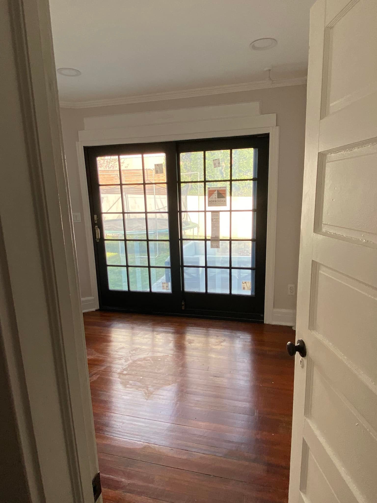Interior room with hardwood floors, a black-framed glass door, and a partially open white door.
