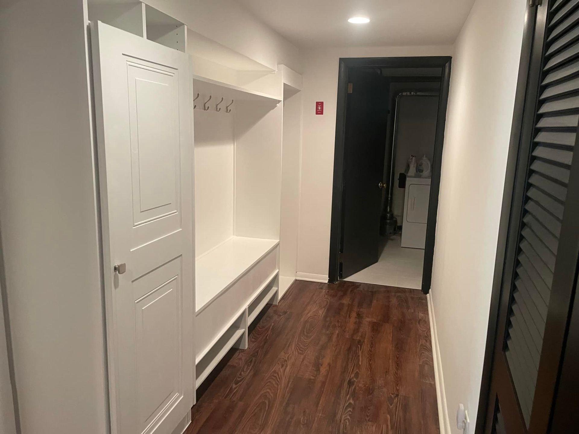 Hallway with built-in white storage and bench. Dark wood flooring, black door, and a louvered black door.