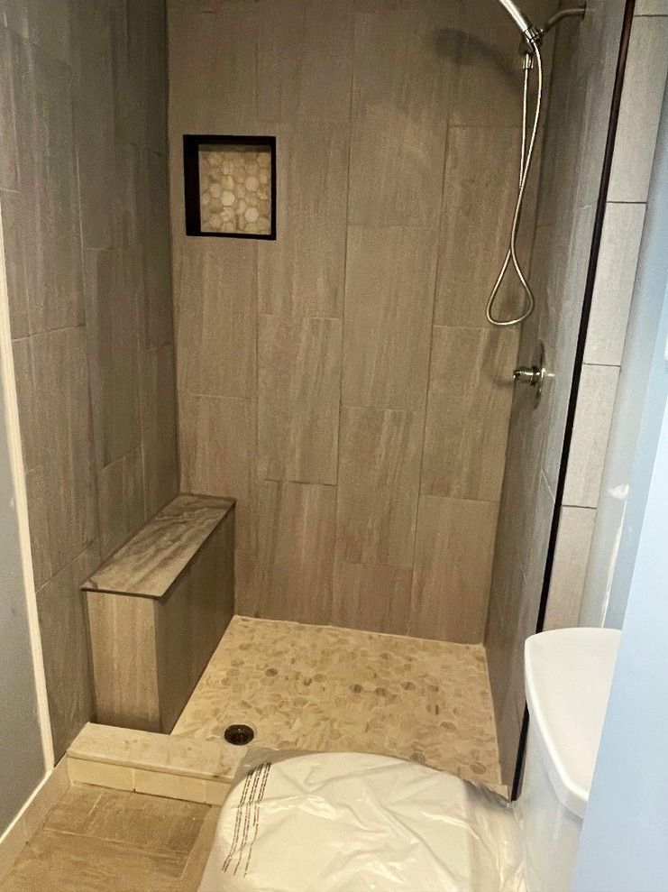 Shower with built-in bench, gray tile walls, and a recessed niche with decorative tile. A toilet is in the foreground.