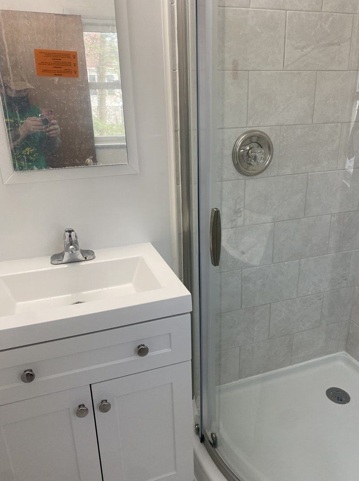 Bathroom with white vanity, sink, mirror, and shower with light gray tiled walls.