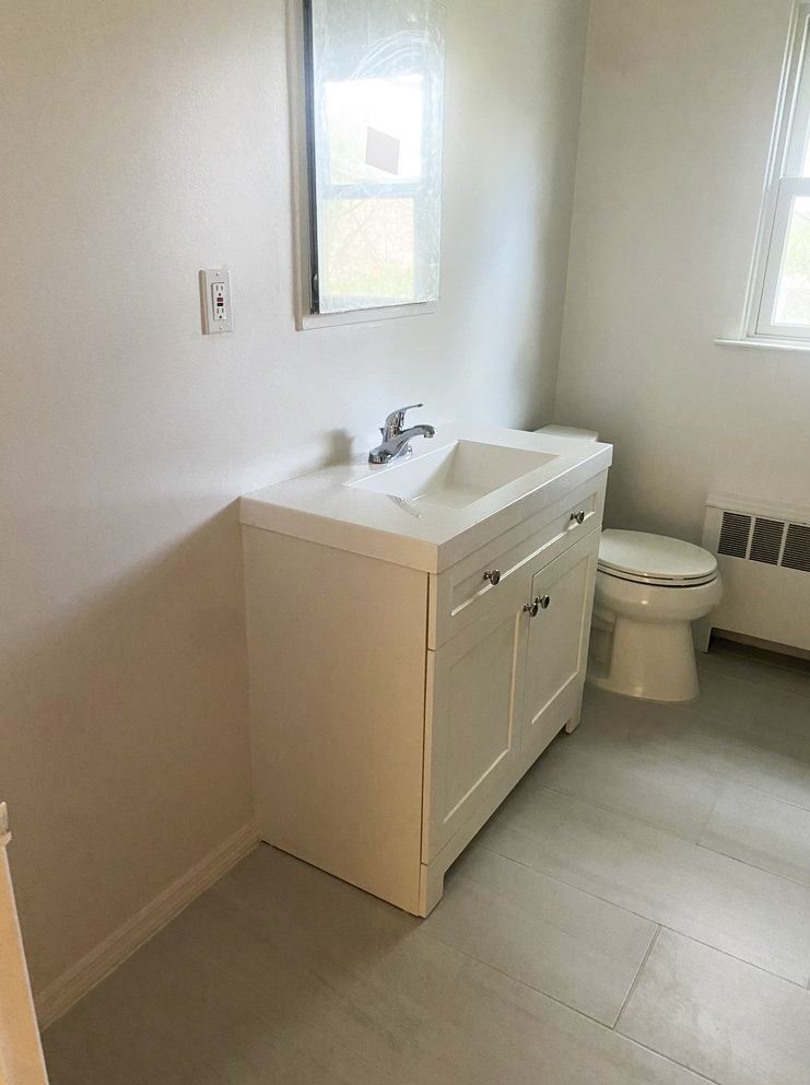 Bathroom with white sink cabinet, toilet, and window.