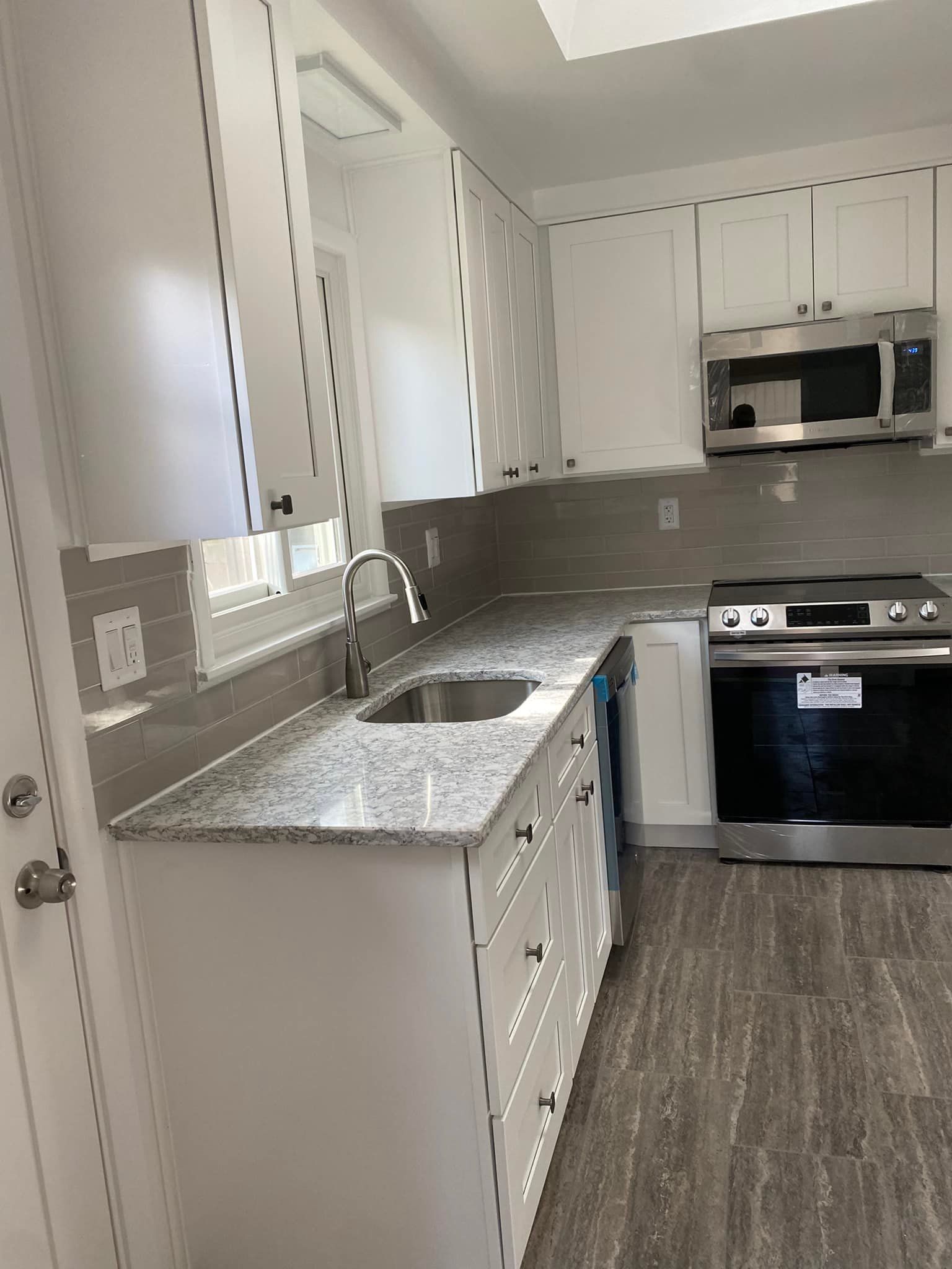 White kitchen with gray countertops, stainless steel appliances, and gray backsplash.