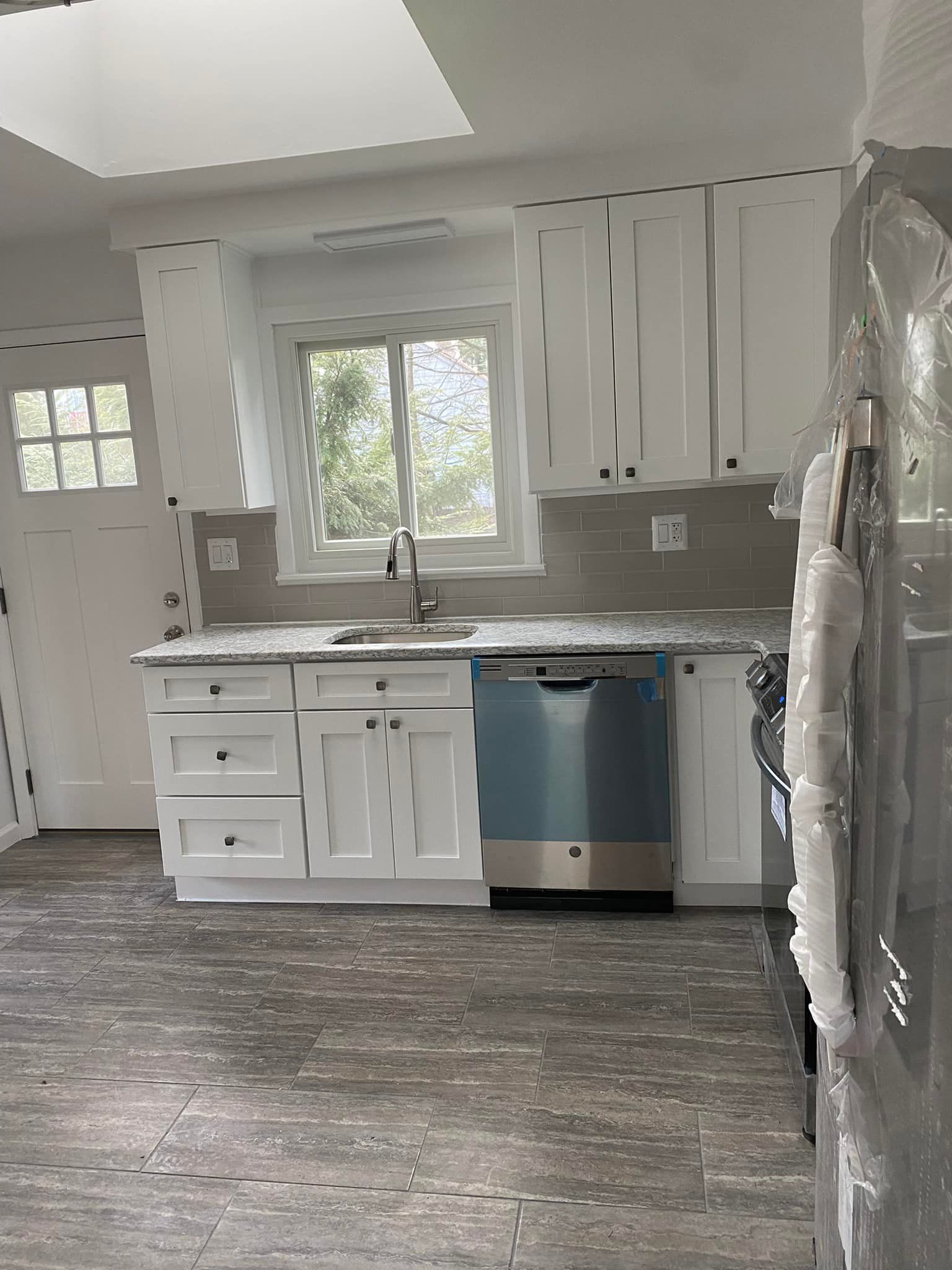 White kitchen cabinets with gray countertops and appliances; view of window and door.