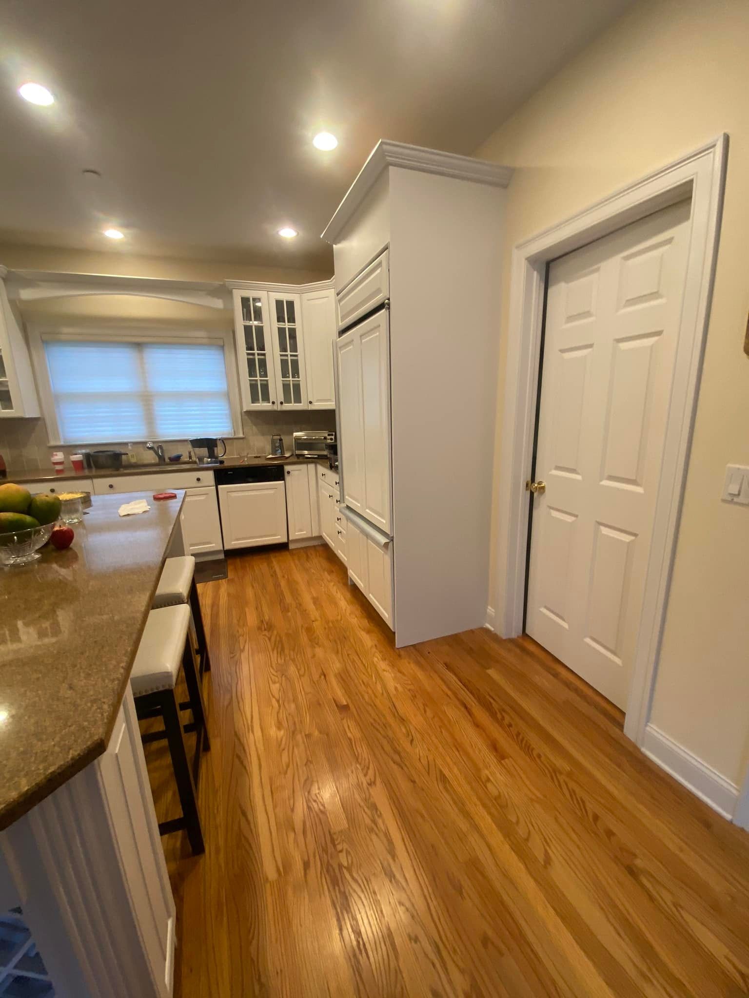 Kitchen with white cabinets, refrigerator, wooden floors, and a door.