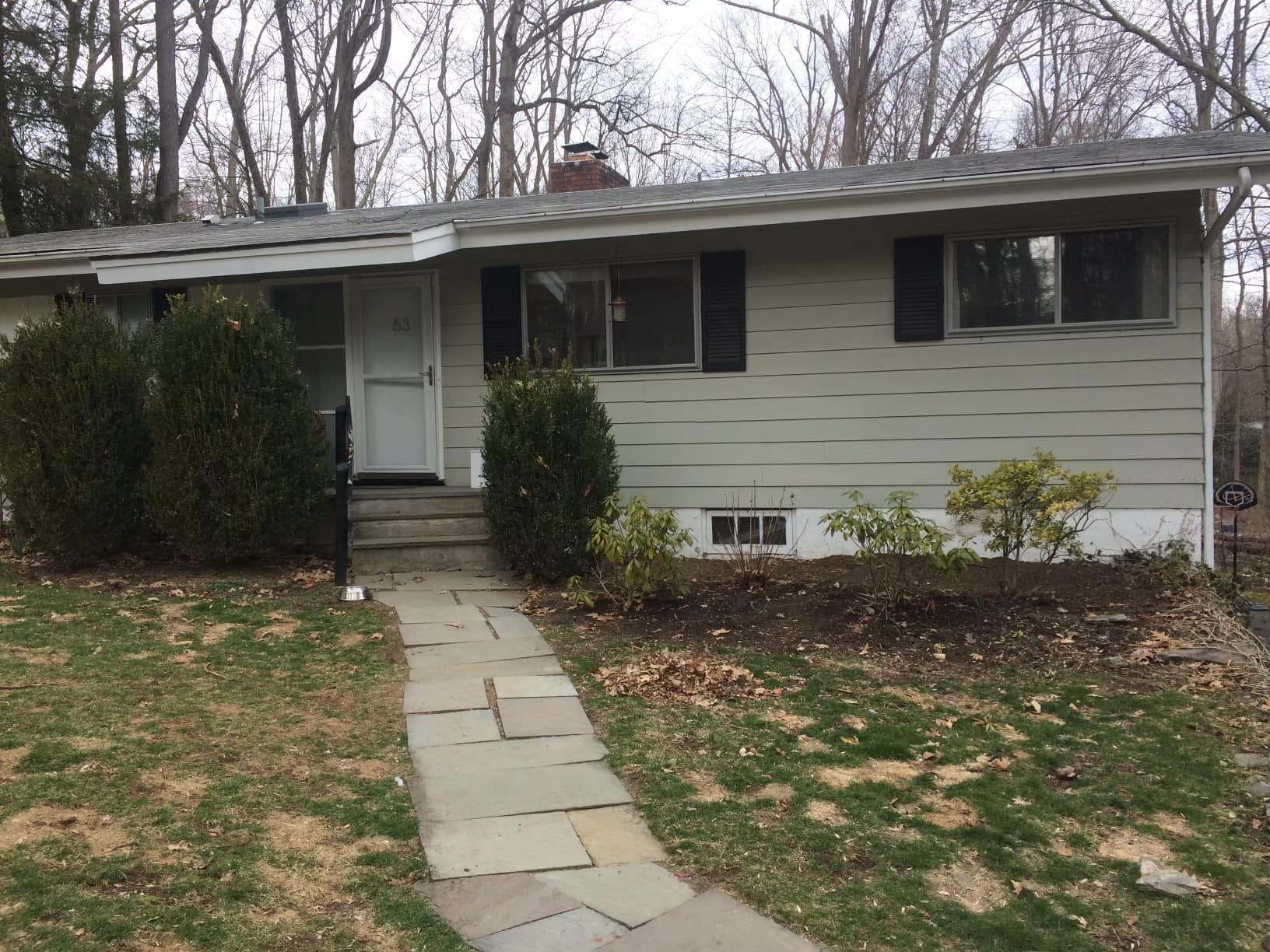 Light green ranch house with stone path, bushes, and bare trees in the yard.