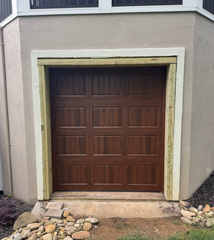 A new wooden garage door installed in a stucco wall opening, framed with pressure-treated lumber.