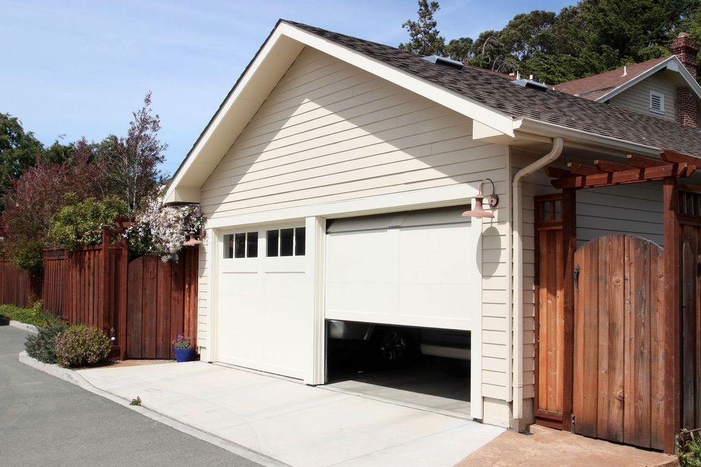 A residential garage with cream-colored siding, a closed left door, and a partially open right door on a sunny day.