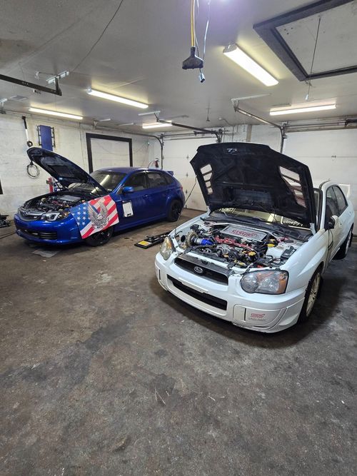 Mechanic in blue jumpsuit using a laptop to diagnose a red car's engine.