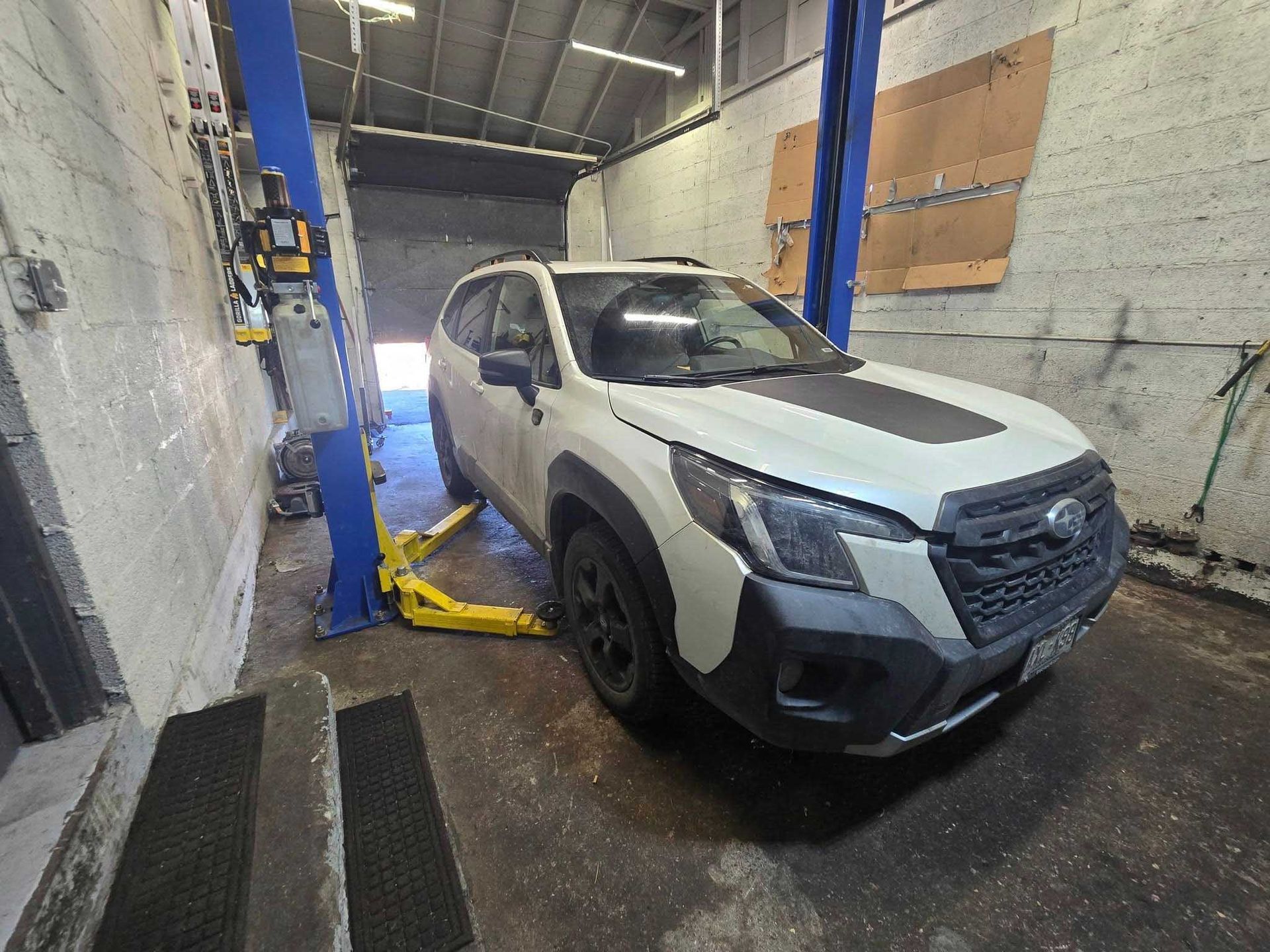 White Subaru Forester SUV on a car lift in a garage.