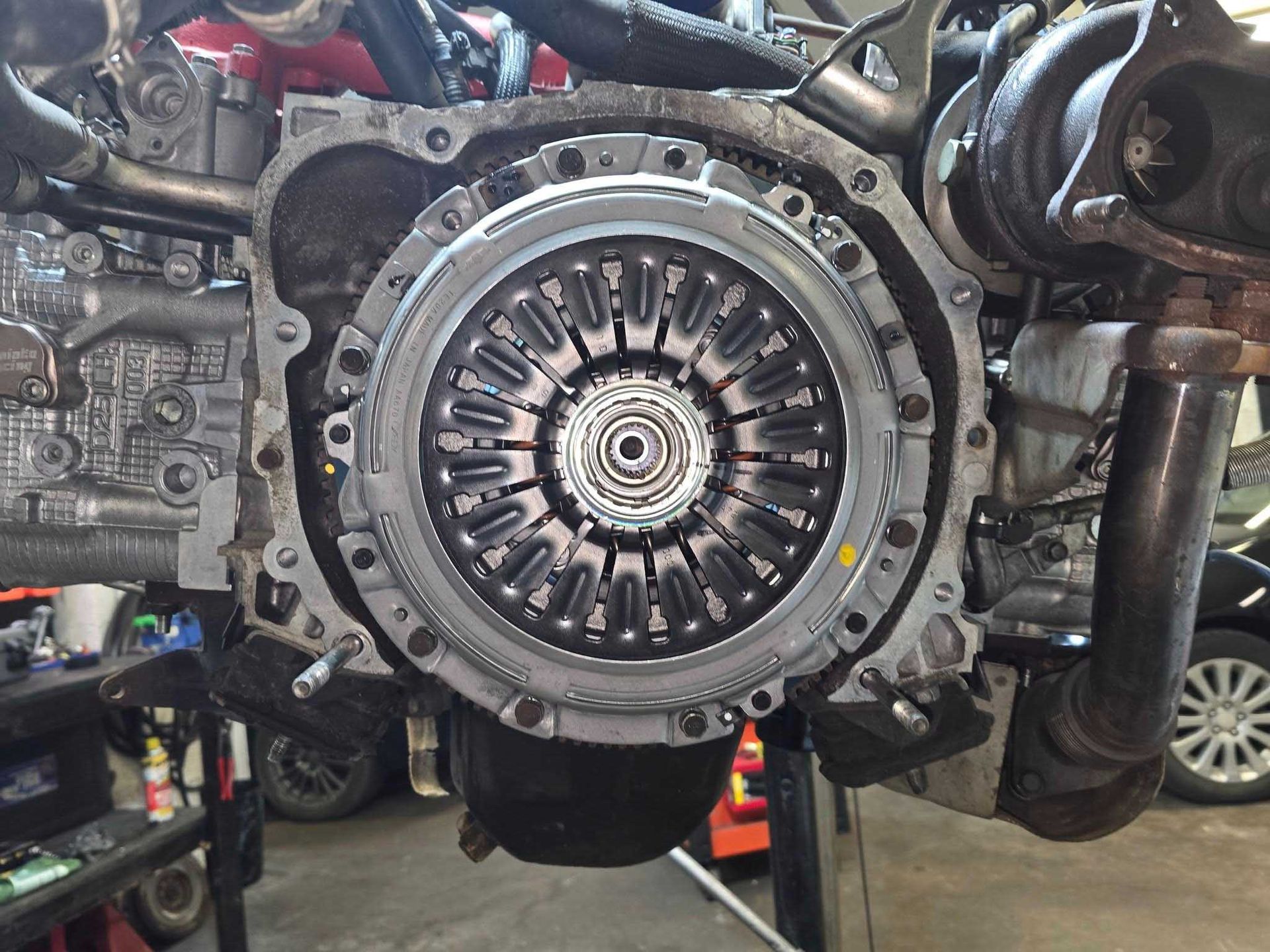Engine block with a clutch assembly installed, viewed from the front, in a garage.