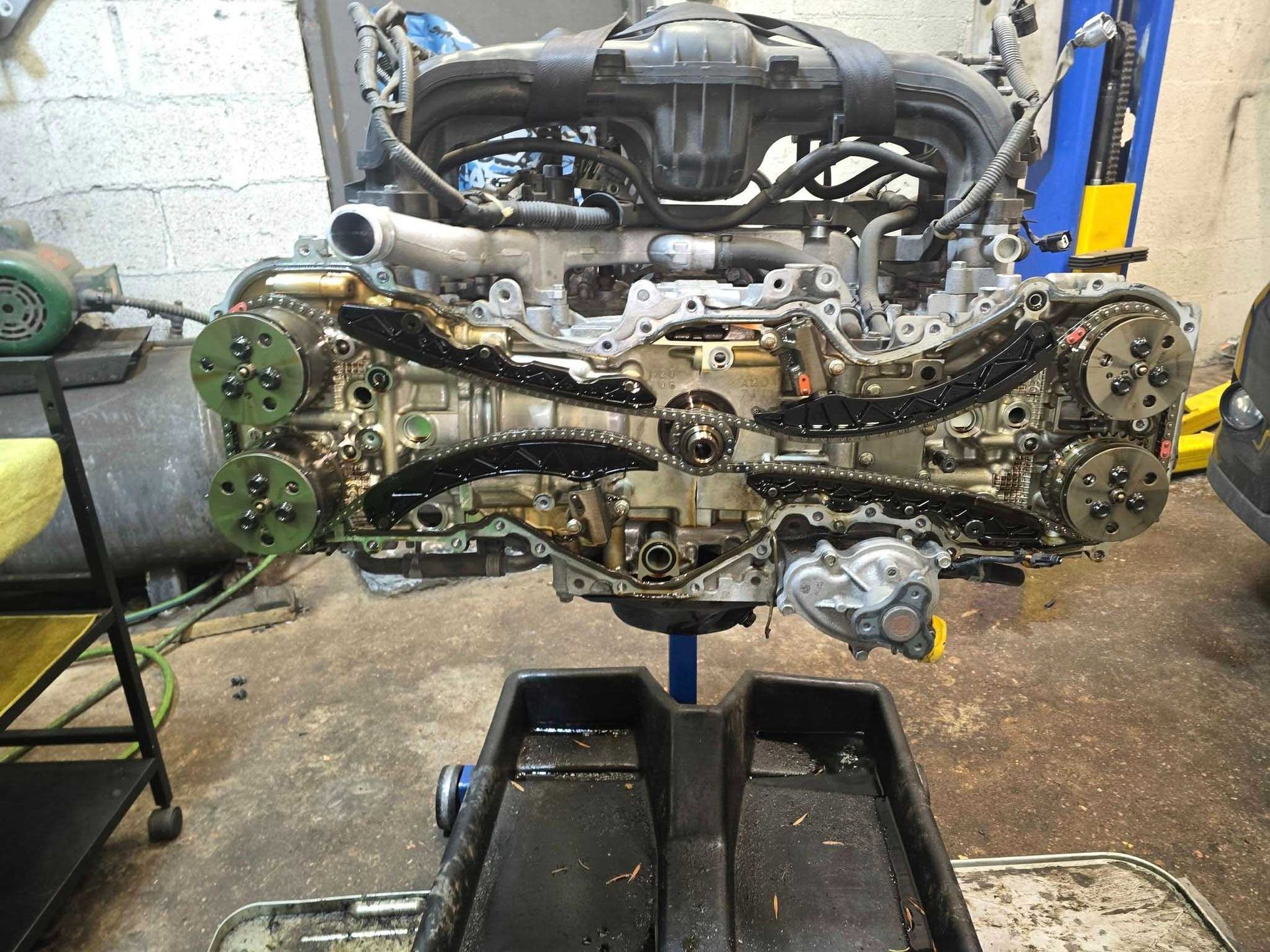 Subaru engine, partially disassembled, showing timing chains and internal components in a garage setting.