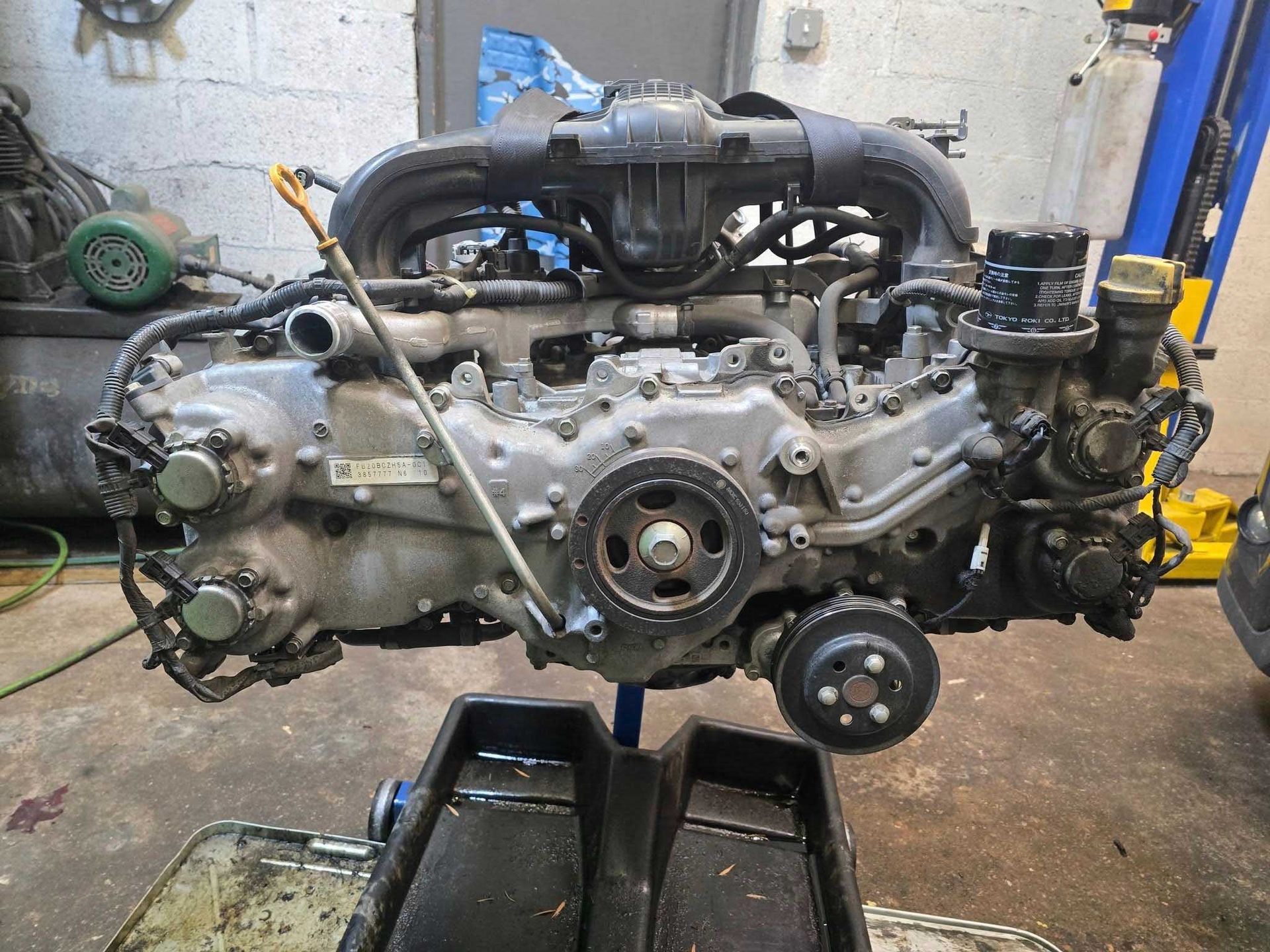 Subaru engine, removed from a vehicle, resting on a stand in a garage.