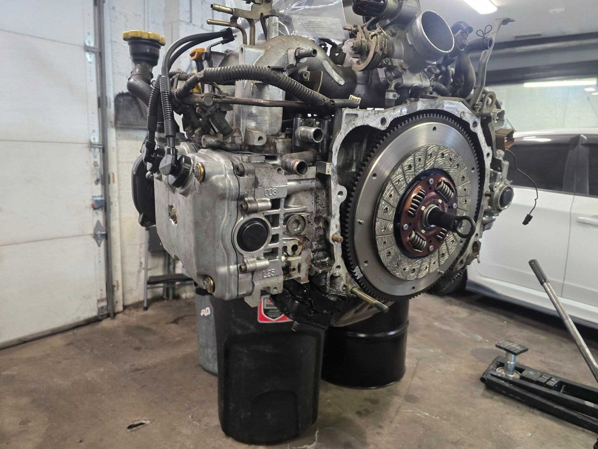 Engine of a vehicle, mostly gray and silver, on black drums in a garage.