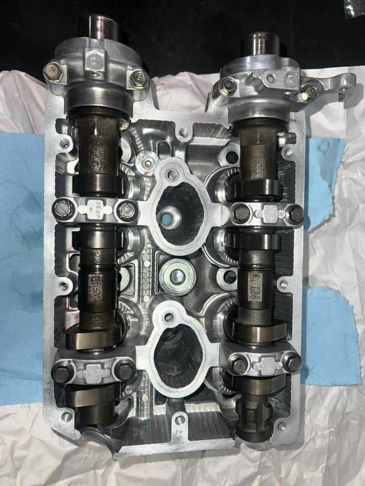 Engine cylinder head with camshafts installed, gray metal with dark components.