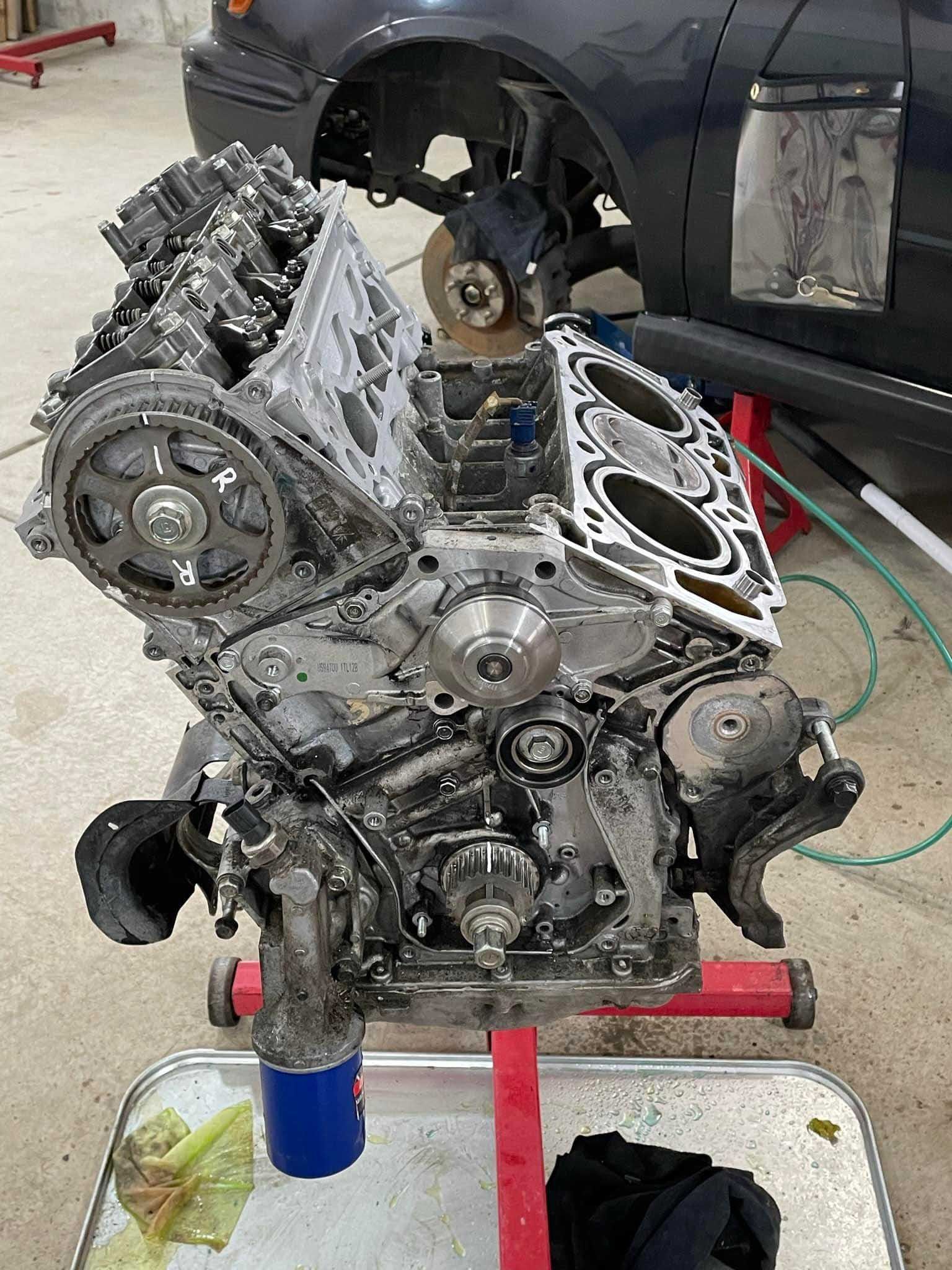 Engine block on a stand, partially disassembled, with timing belt components visible.