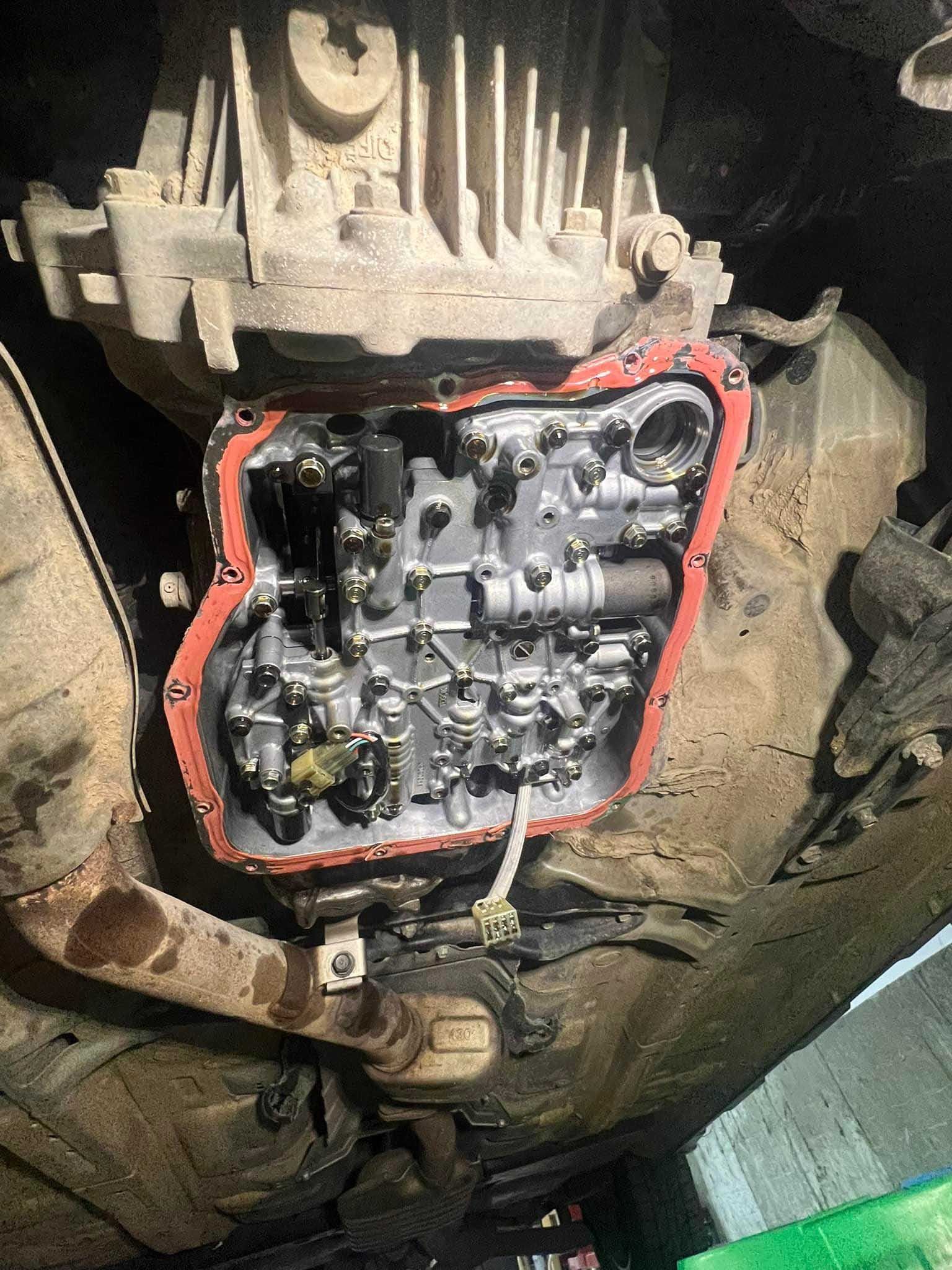 Underside view of a vehicle's exposed automatic transmission with the pan removed, revealing internal components and a red gasket.