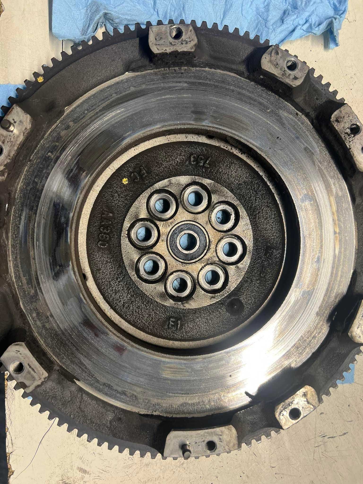 Flywheel with gears and bolt holes, likely from a vehicle. Metal, worn condition.