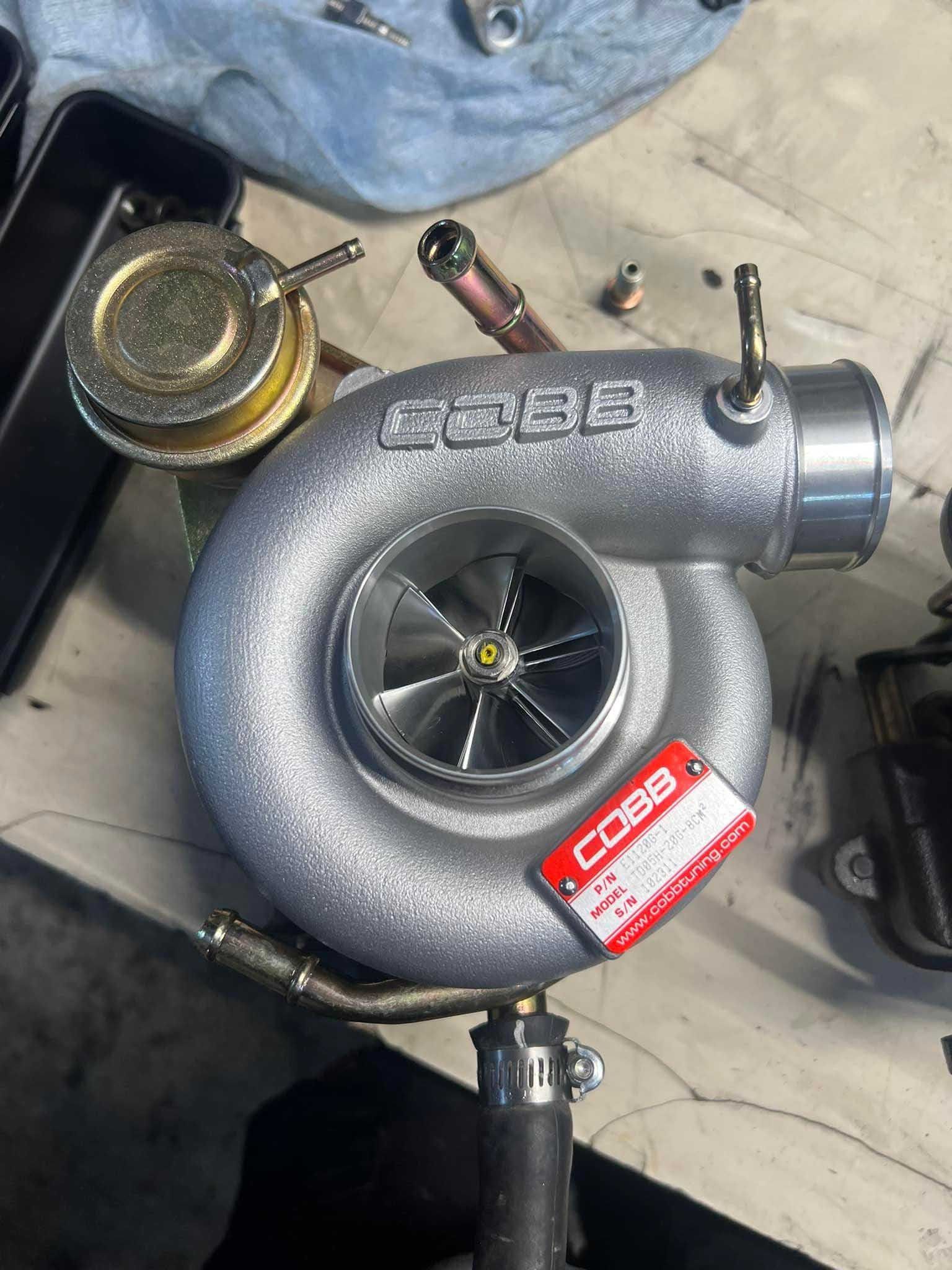 Silver Cobb turbocharger with a red tag, sitting on a surface.