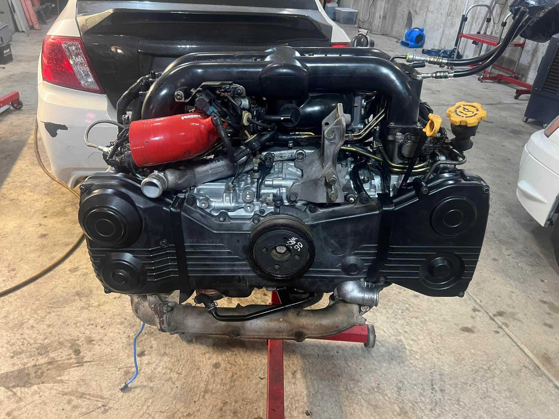 Subaru engine on a red stand, black and silver components, red air intake, garage setting.