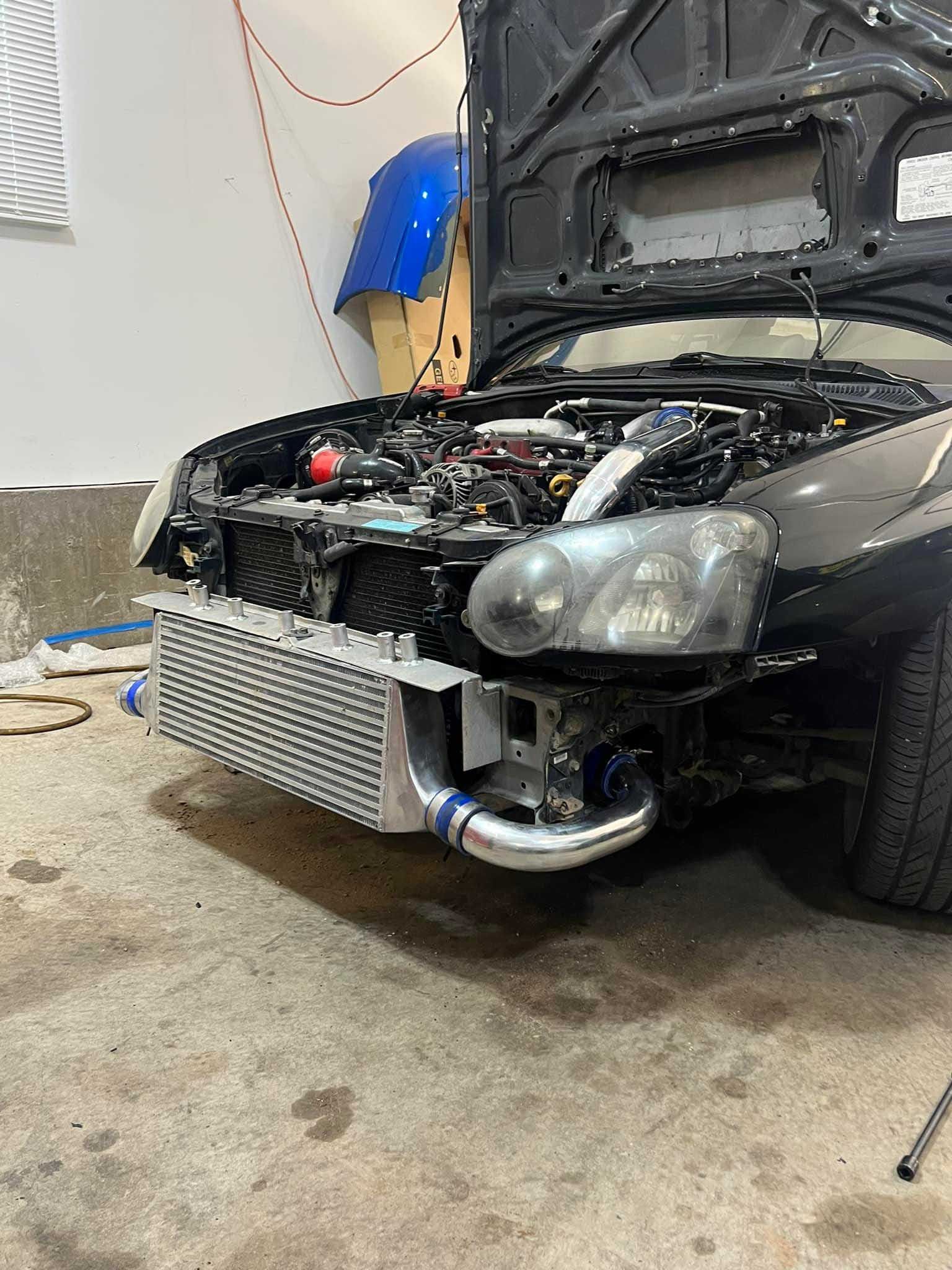 Black car with open hood, intercooler and turbo installed in garage.