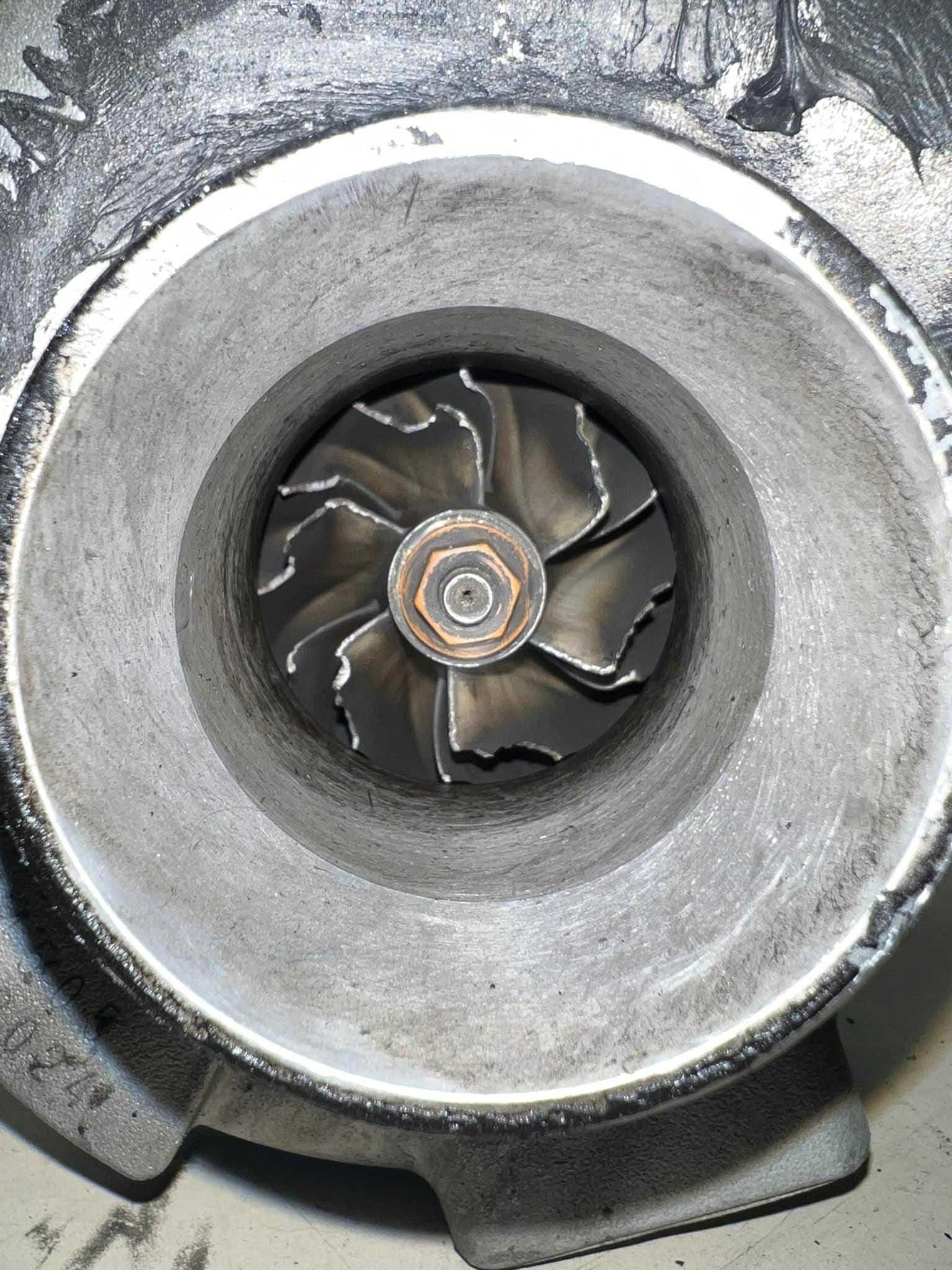 Close-up of a damaged turbocharger impeller. Blades show wear and black soot.