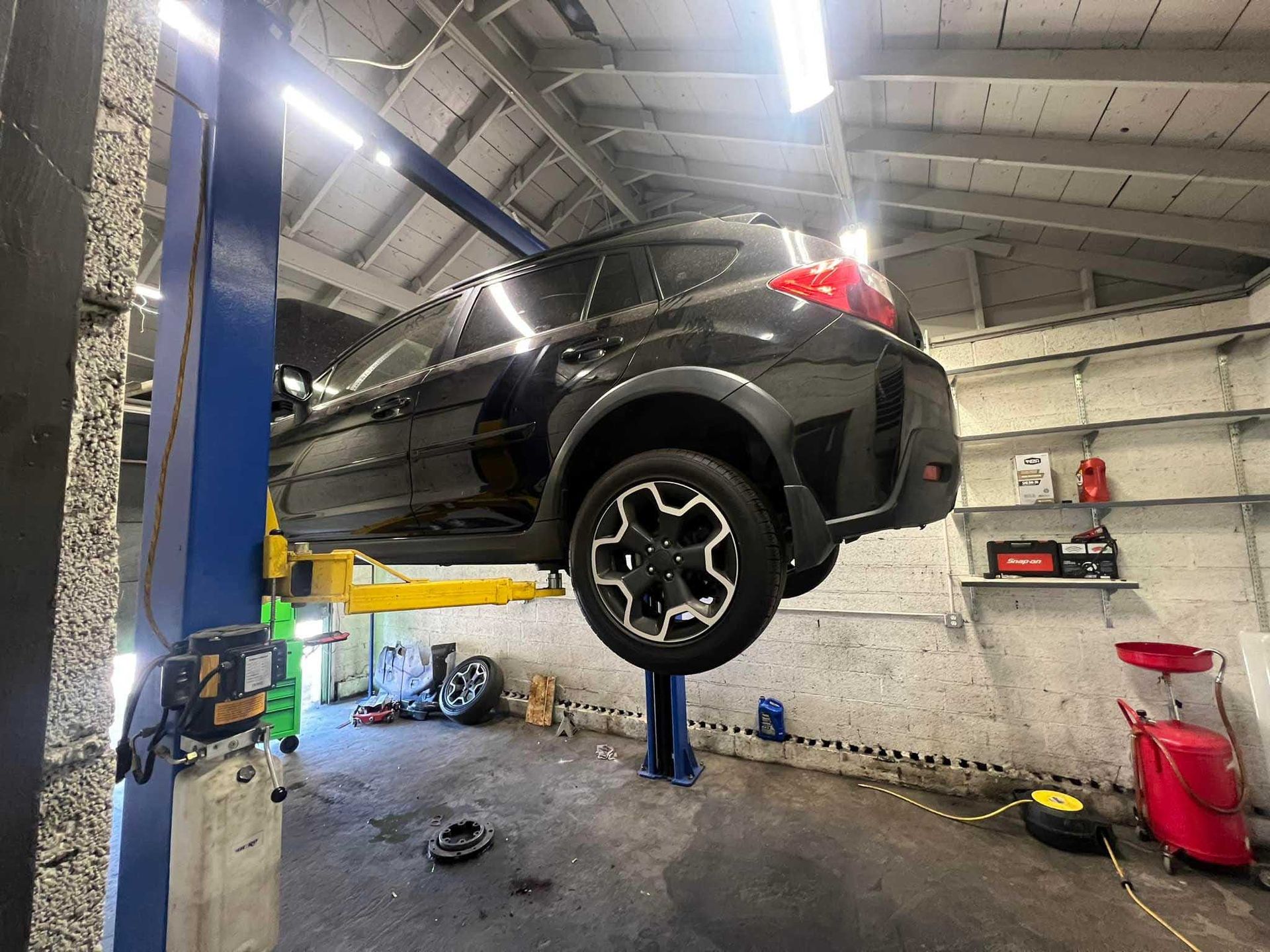 Black SUV lifted on a blue hydraulic lift inside a garage; equipment and tools visible.