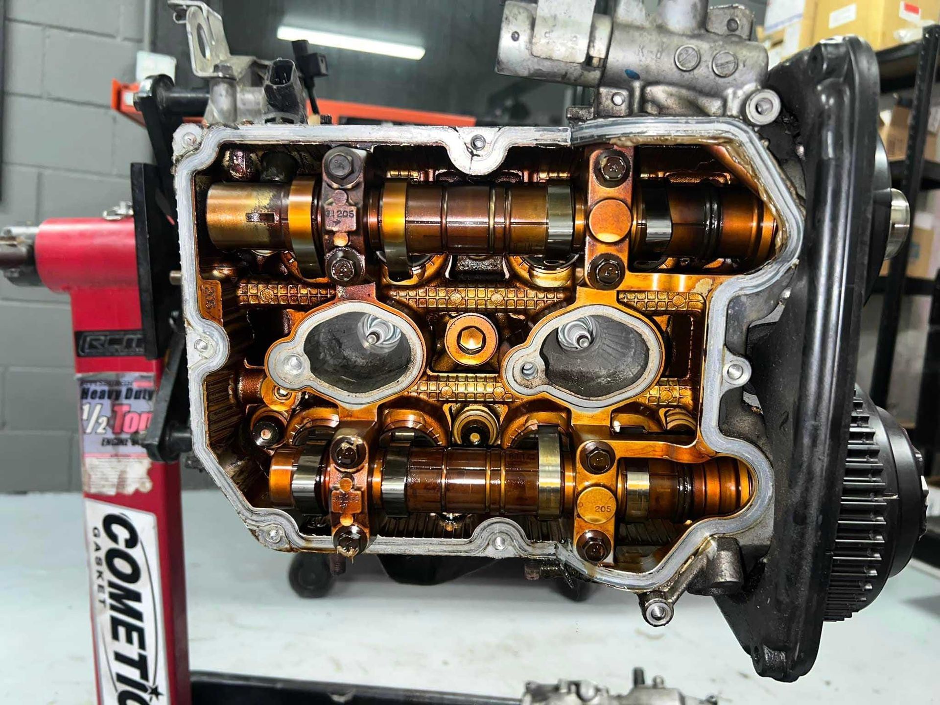 Open engine with visible camshafts and oil, mounted on a red engine stand in a workshop.