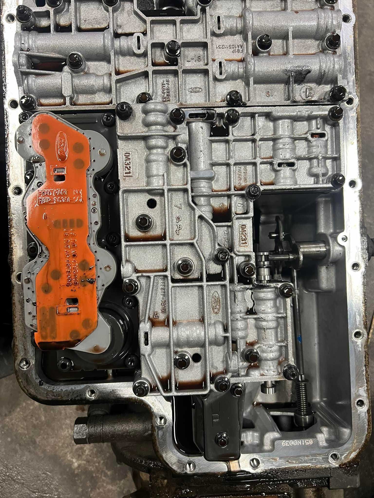 Opened automatic transmission valve body with orange circuit board and various internal components.