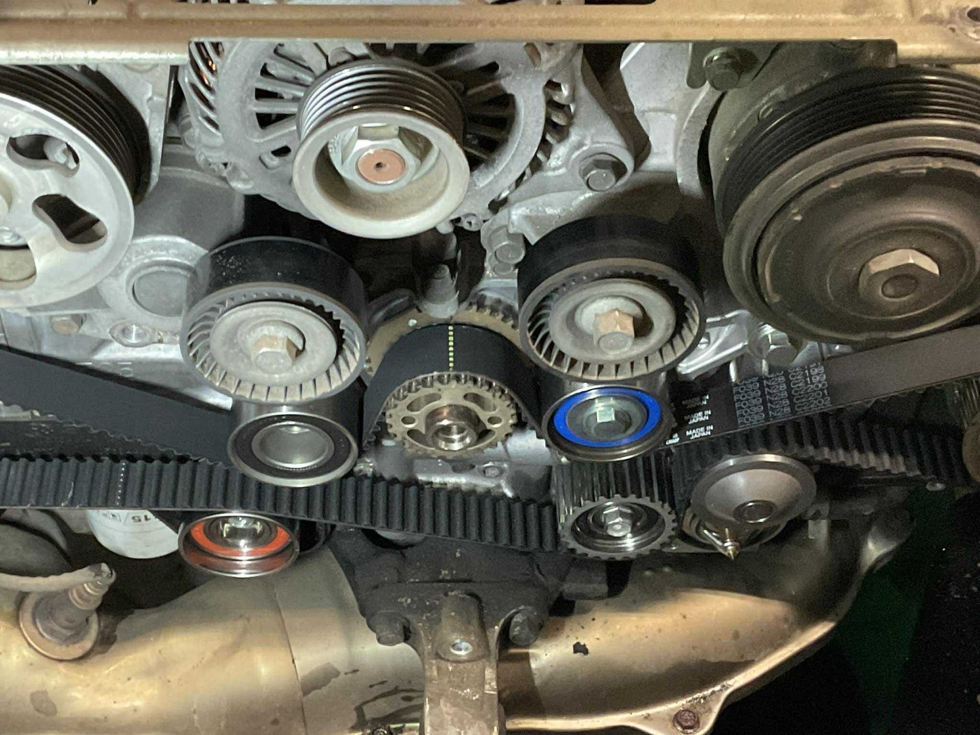 Car engine with belts, pulleys, and timing components visible, likely during maintenance.