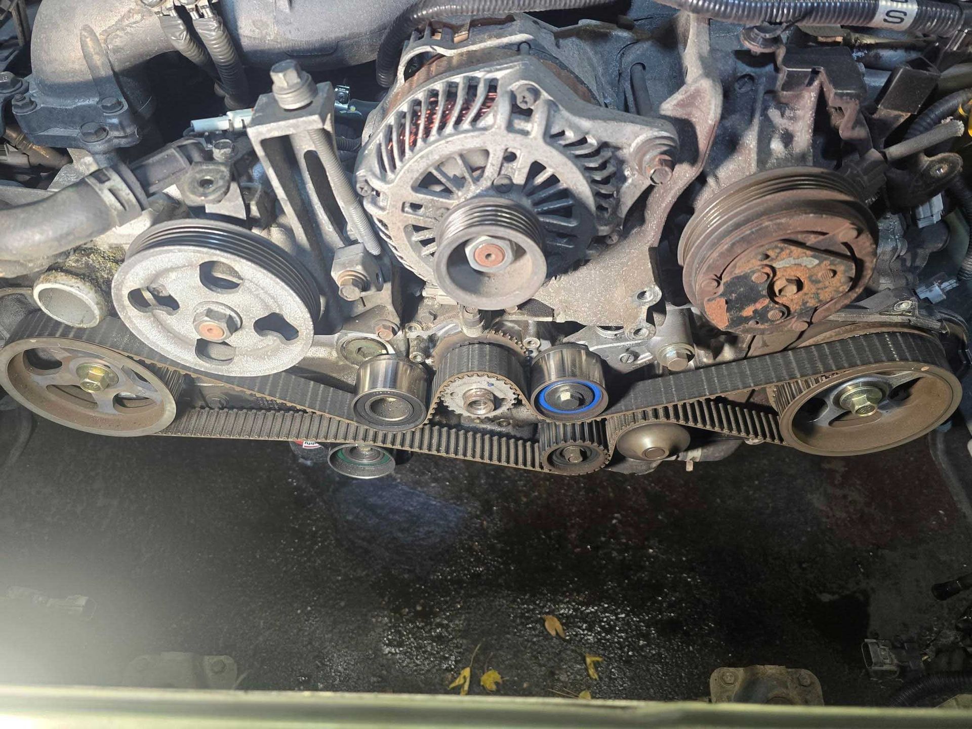 Engine with belts and pulleys, visible timing belt, and alternator in an automotive setting.