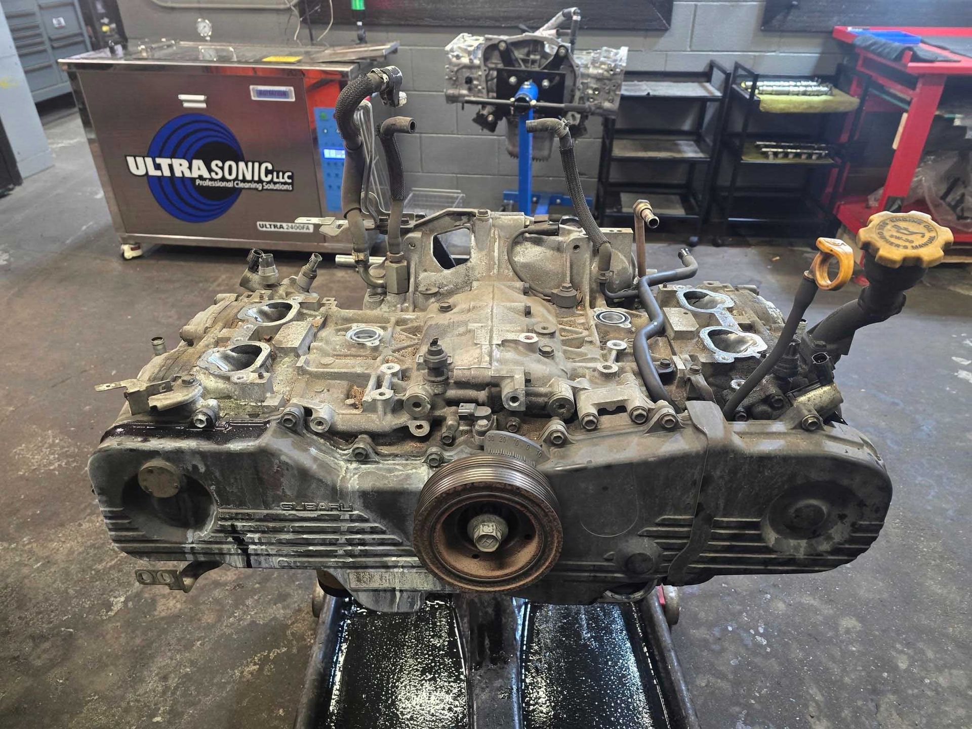 Subaru engine, partially disassembled, on a stand in a garage.