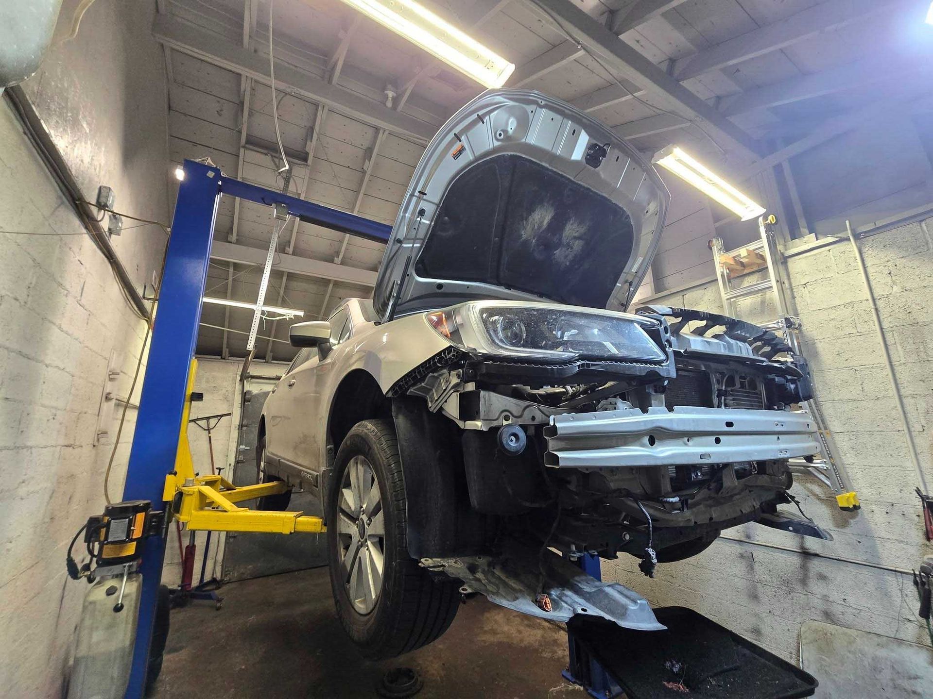 Silver car with open hood on a lift in a garage, front bumper damaged.