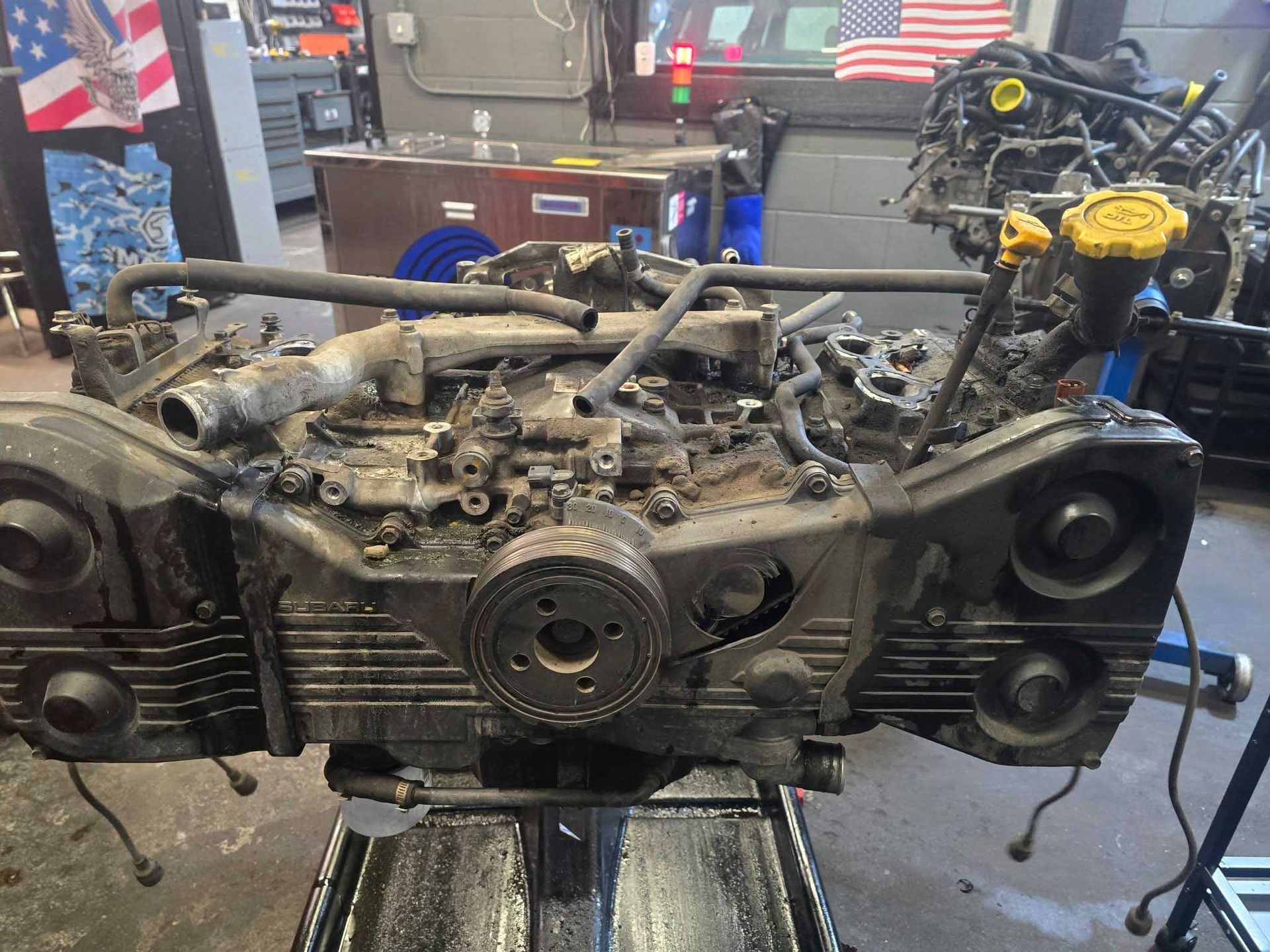 Subaru car engine on a stand in a garage, covered in dirt and grime.