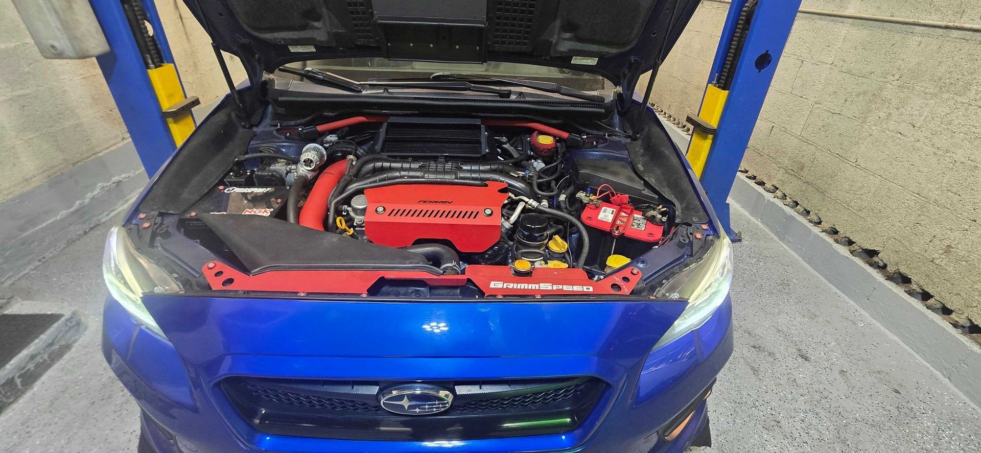 Blue Subaru engine bay with red details. Hood open, car on a lift.
