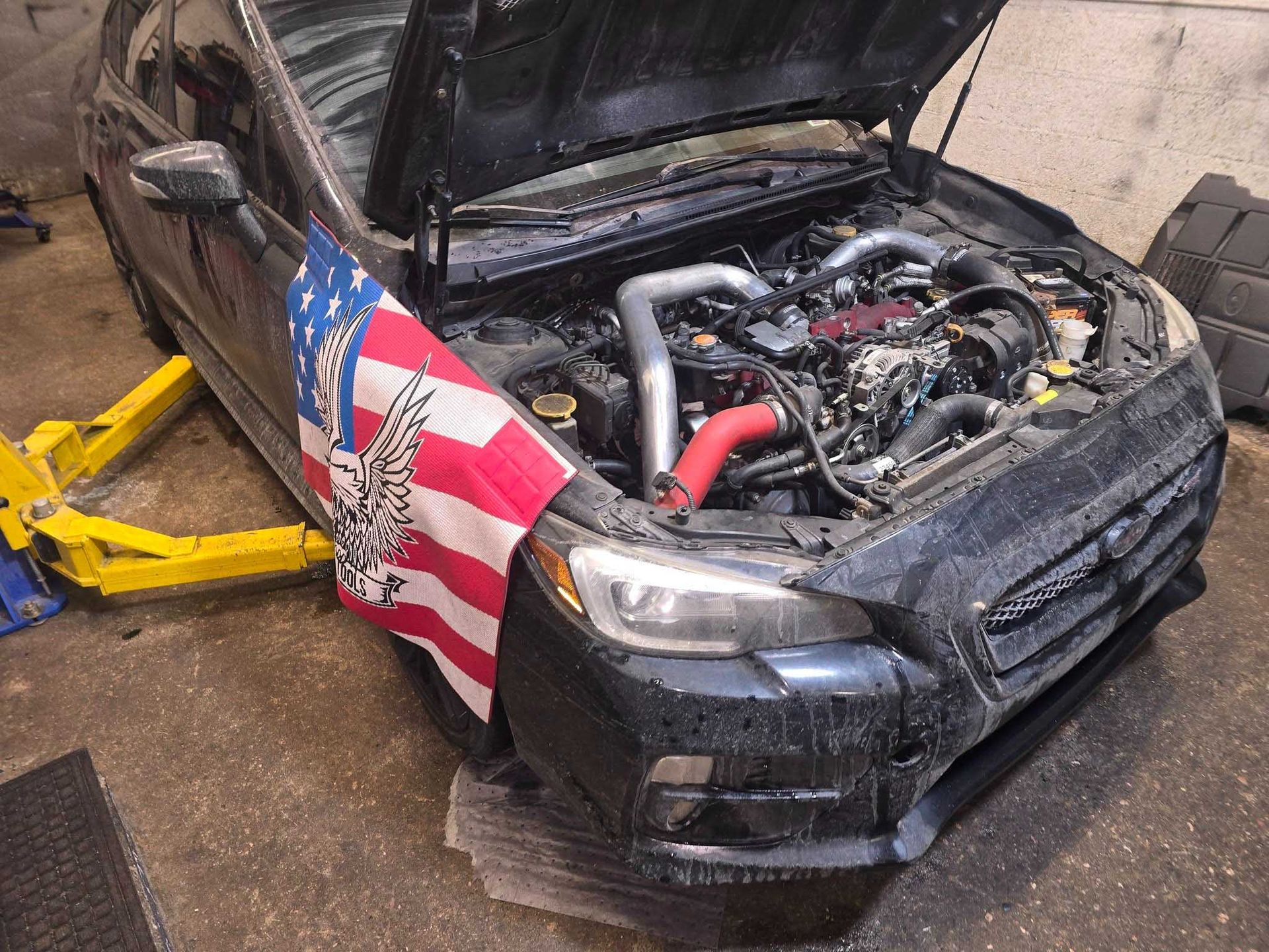 Black car with open hood, being worked on, US flag on side.
