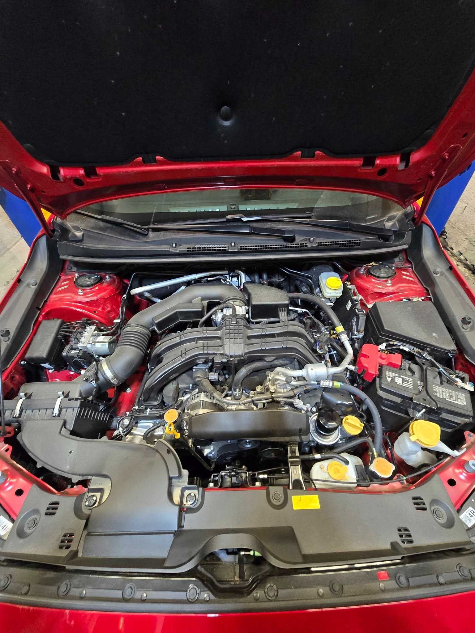 Red car engine bay with black engine, various tubes and components, and a red interior.
