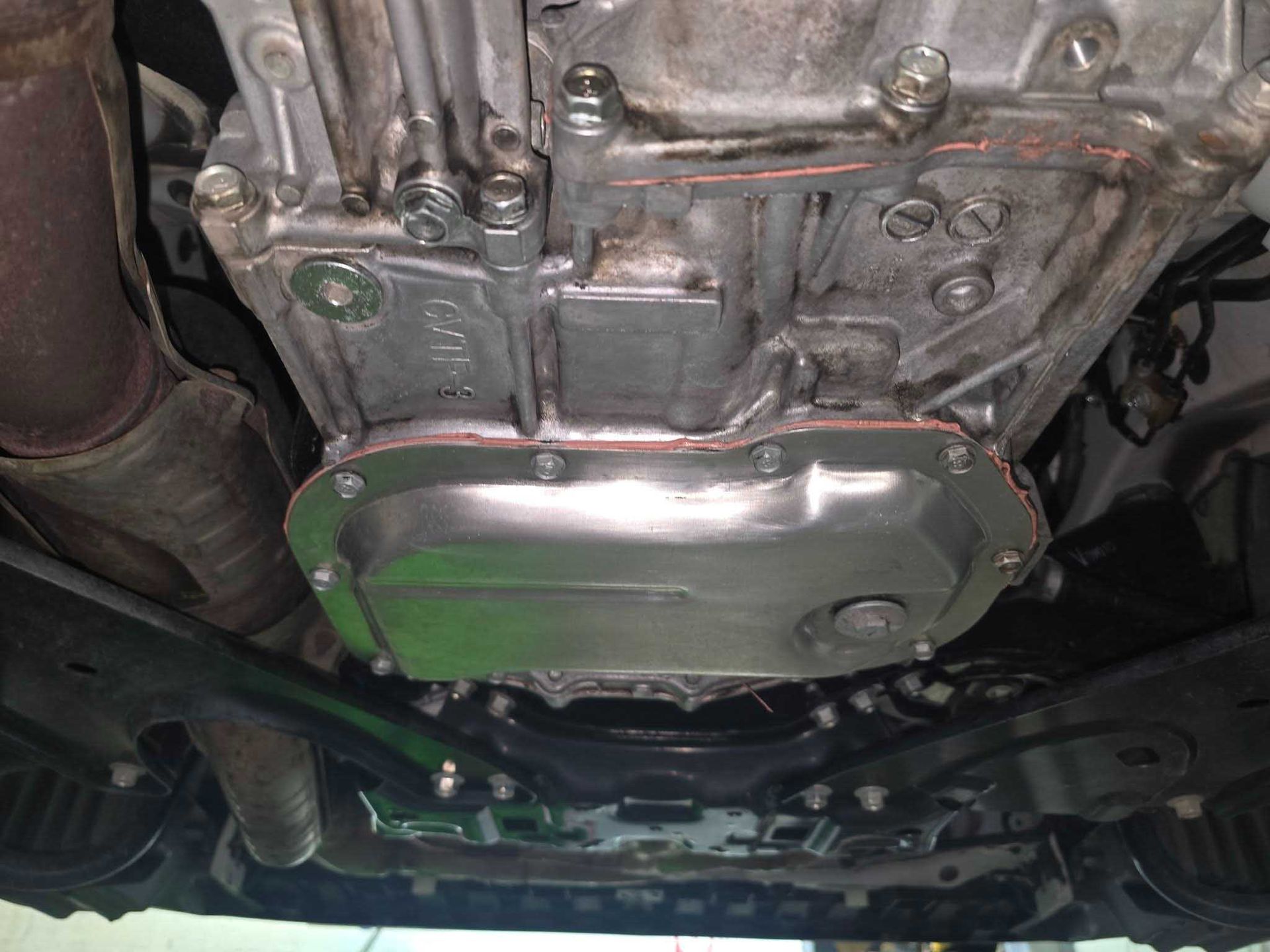 Underside of a car engine showing the oil pan, metallic color, bolts visible.