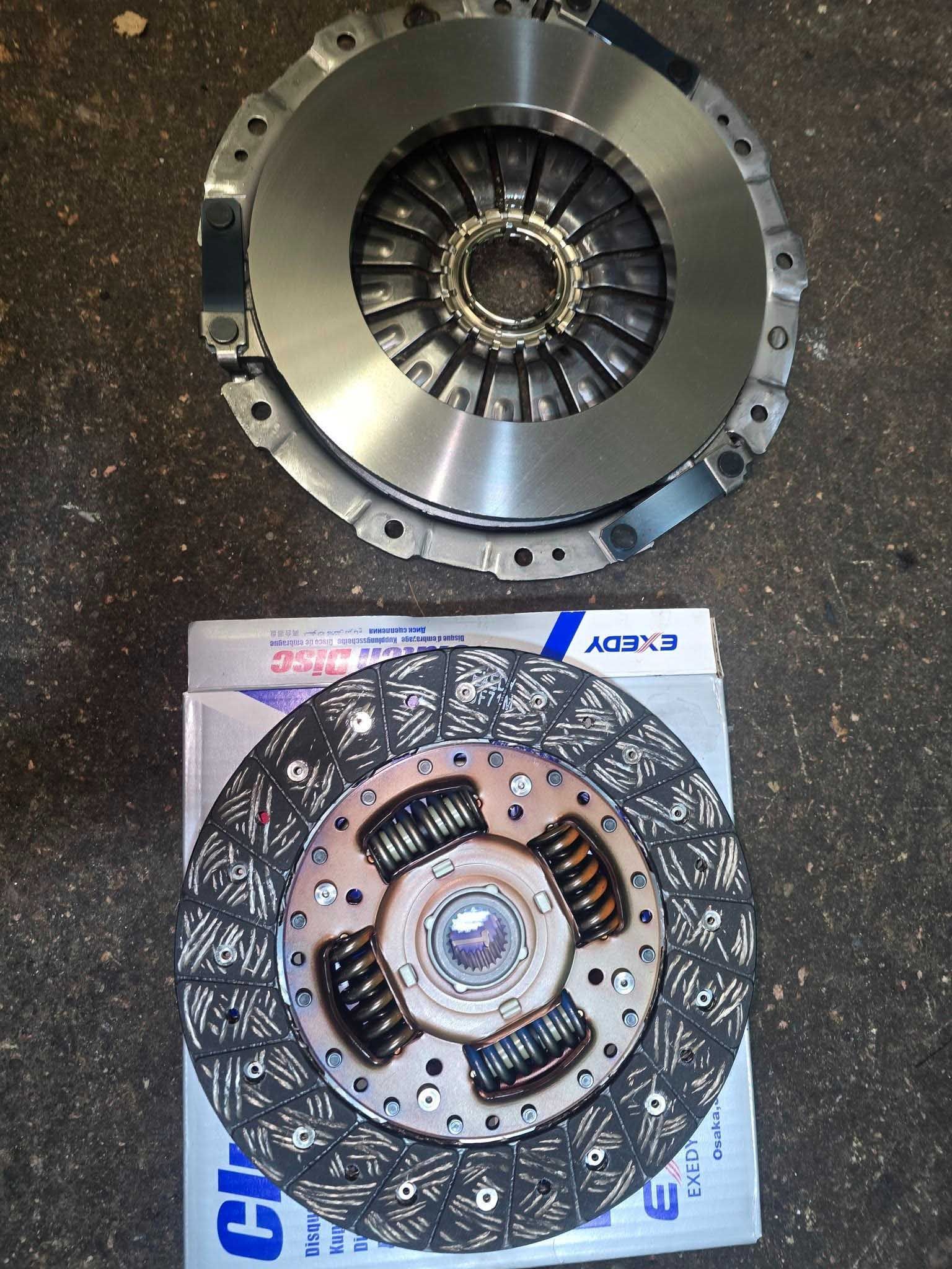 Clutch kit: pressure plate and clutch disc, viewed from above, resting on a box.