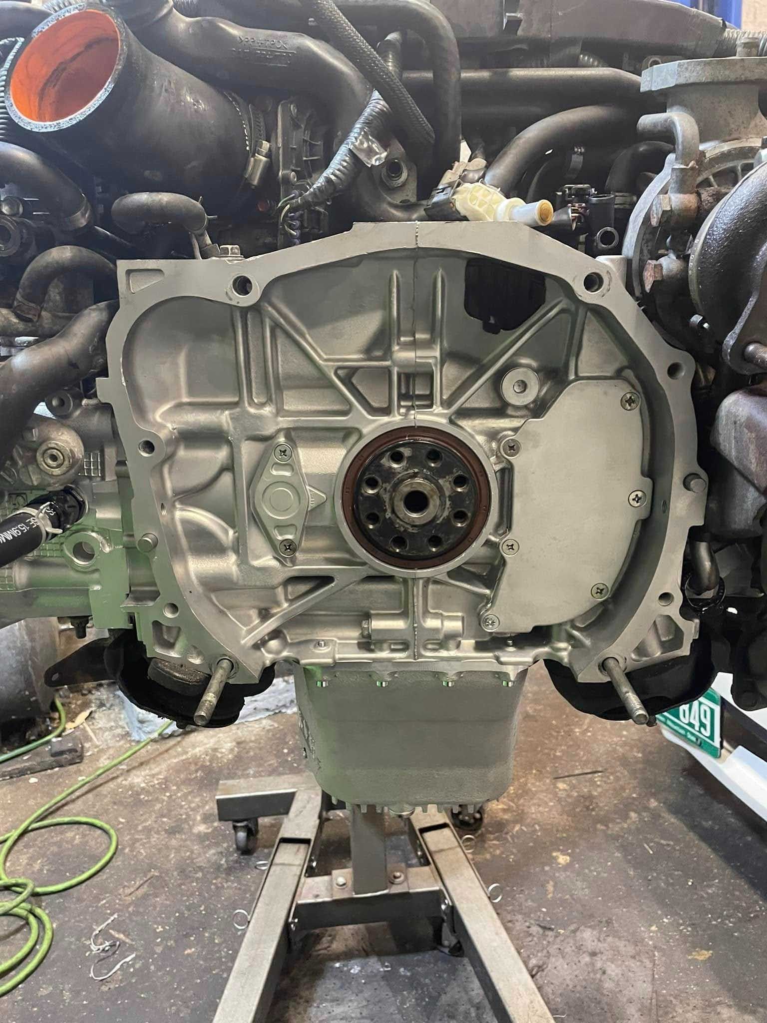 Engine block, open face view, mounted on a stand in a workshop. Gray metal, black components.
