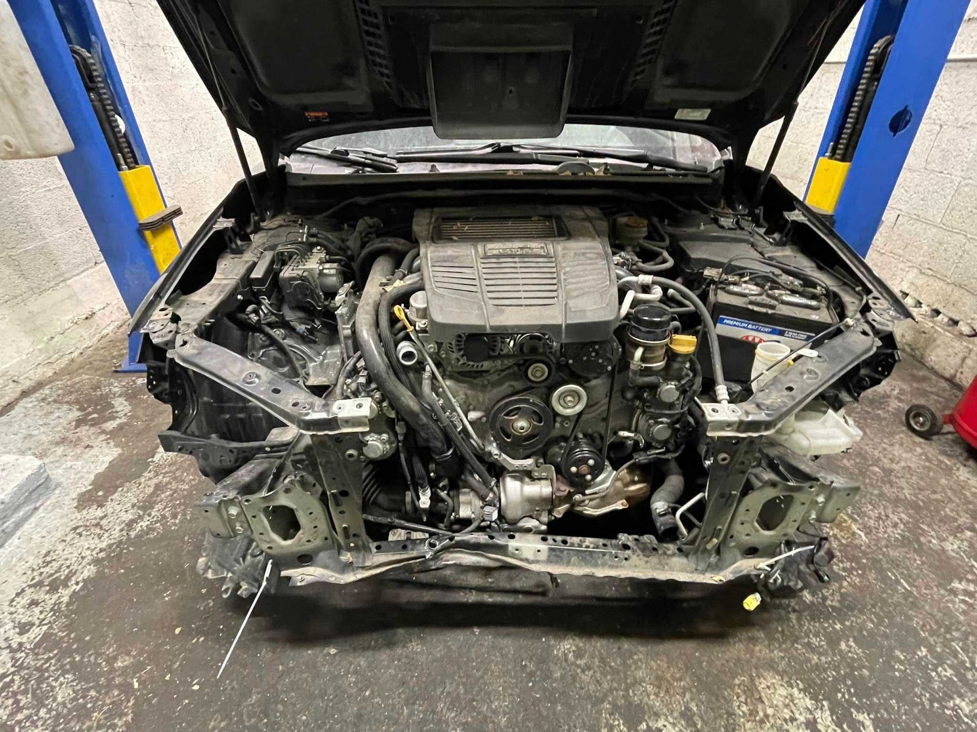 Car engine bay with front body panels removed, open hood, mechanic workspace.