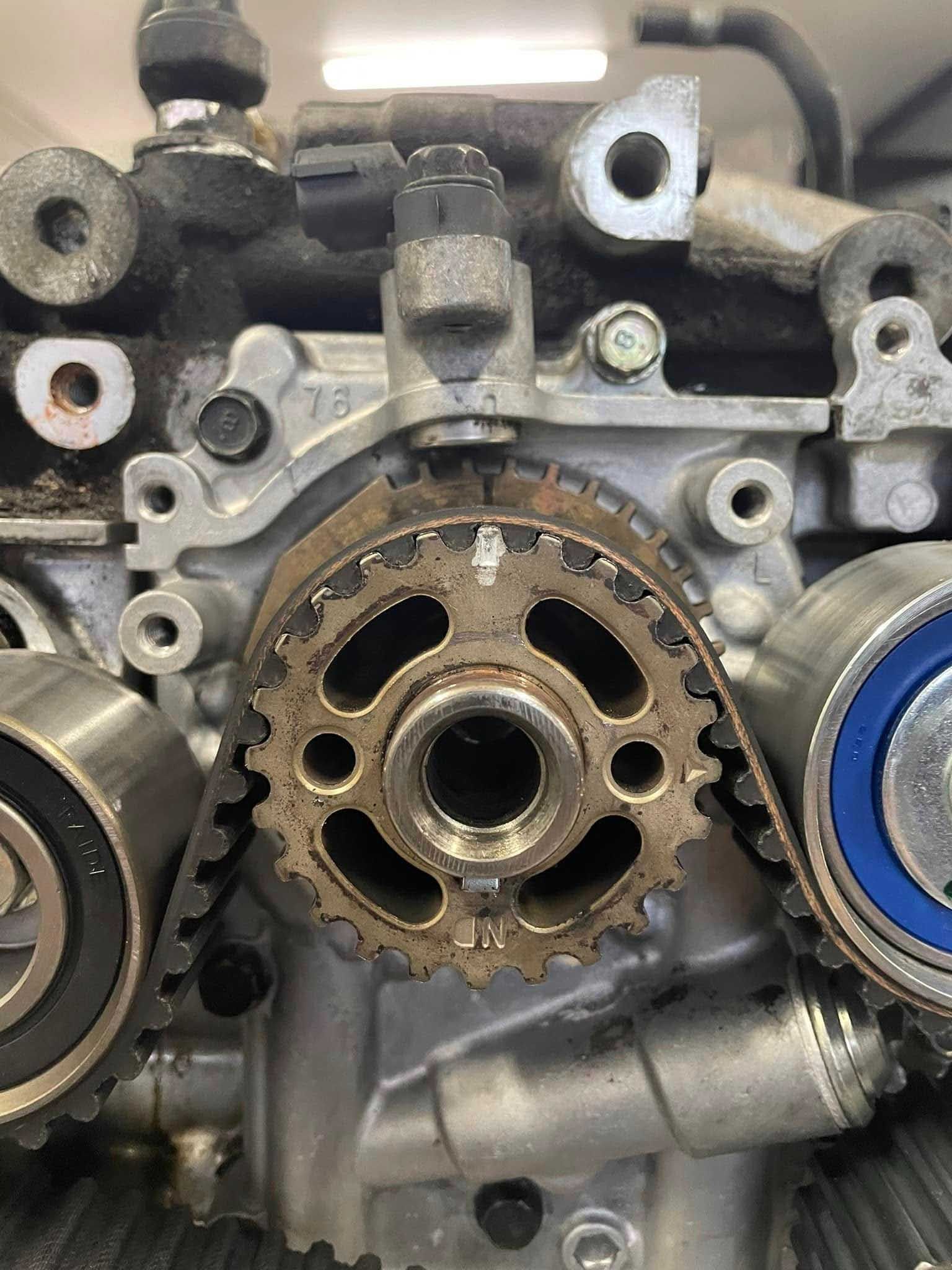 Close-up of a car engine's timing belt and gears, showing components, bolts, and metal parts.