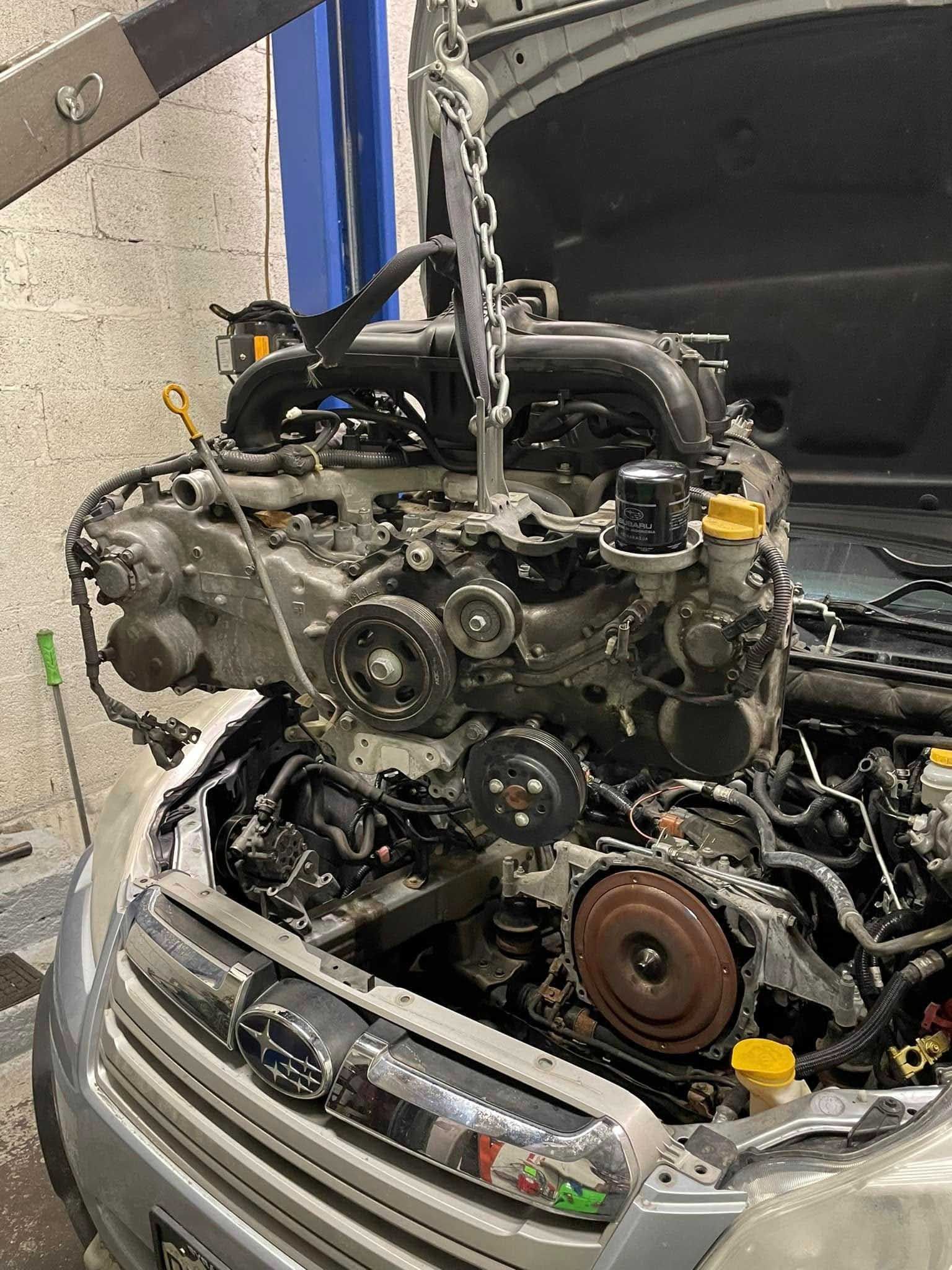 Subaru engine being lifted out of a car in a garage.