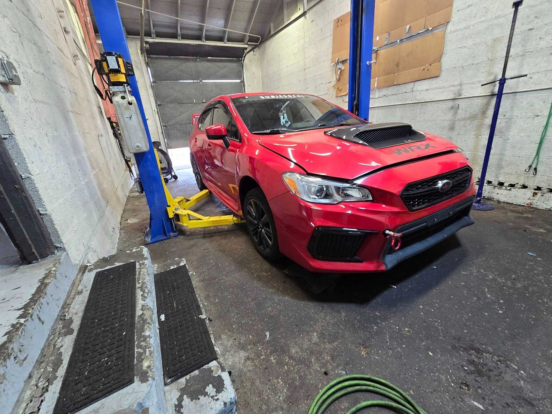 Red Subaru WRX on a car lift in a garage.