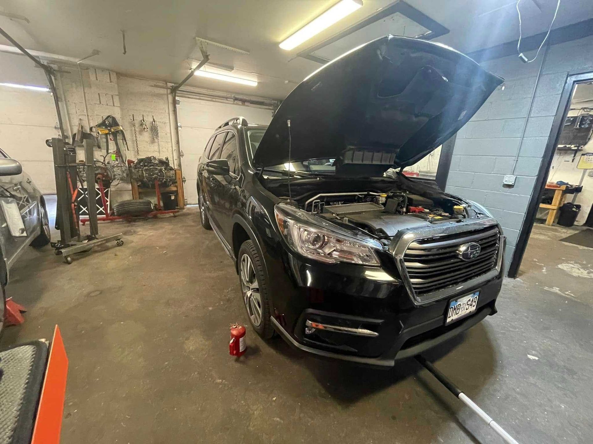Black SUV with its hood up in a garage, red oil container on the ground.